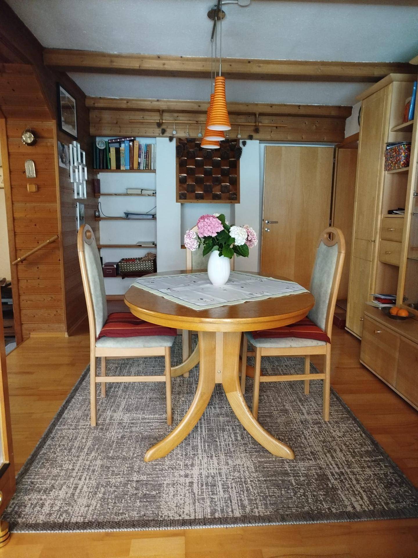 Gemütlicher Essbereich mit rundem Holztisch, Stühlen und einem Bücherregal im Hintergrund.