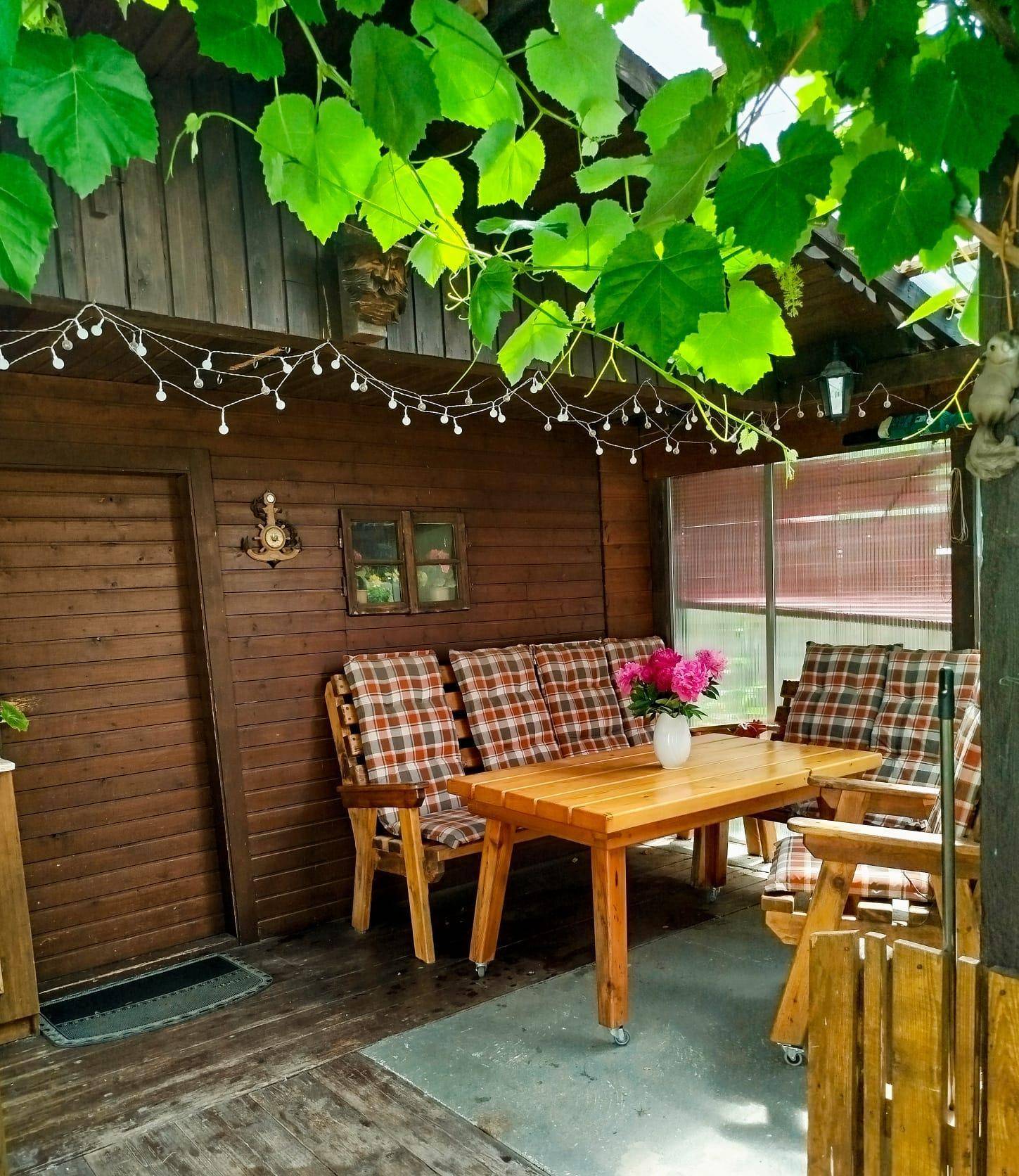 Gemütlicher überdachter Sitzbereich im Freien mit Holzmöbeln und Lichterketten, umgeben von Weinreben.