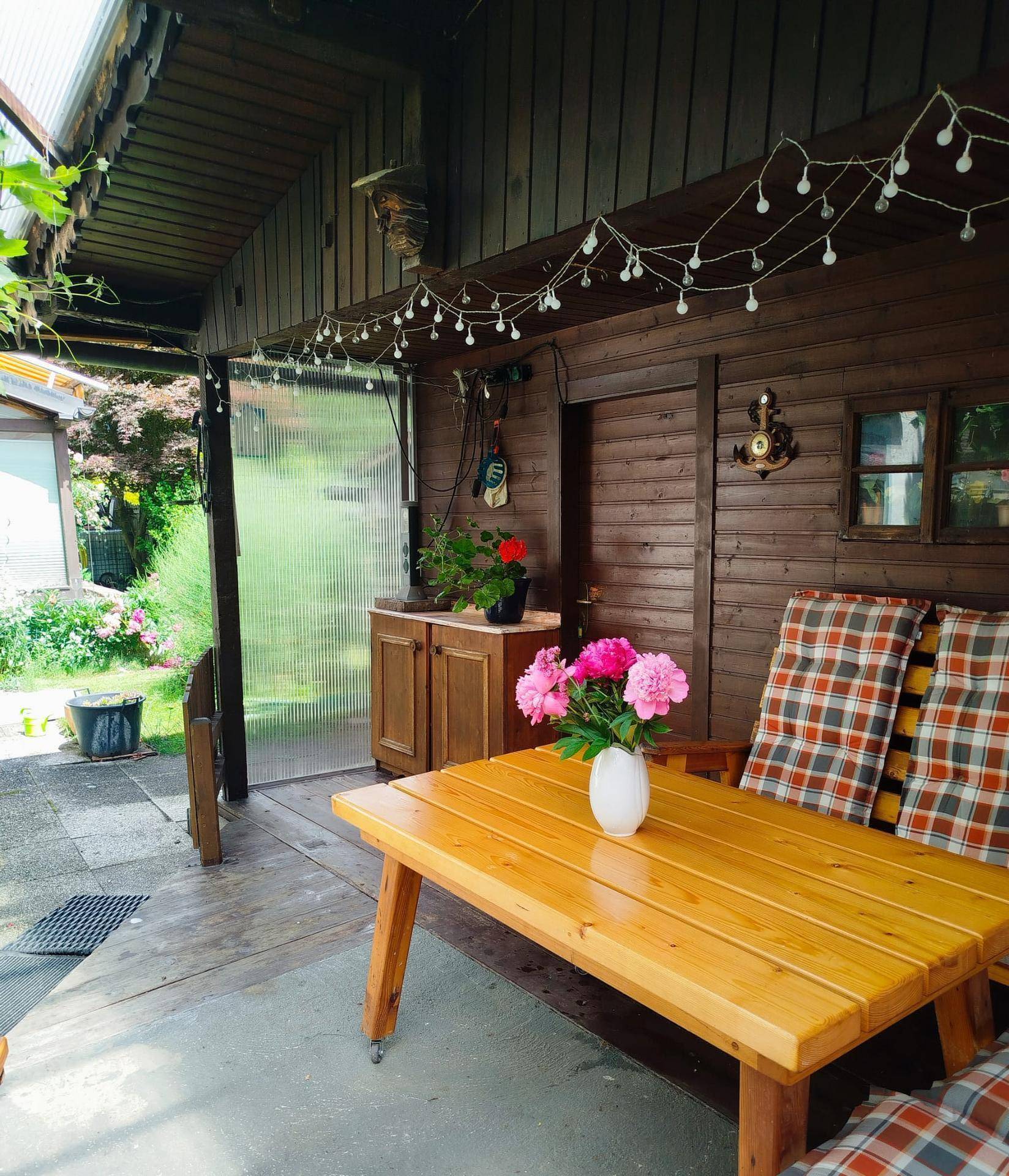 Einladender überdachter Terrassenbereich mit Holztisch, Sitzbänken und Blumen, ideal zum Entspannen.