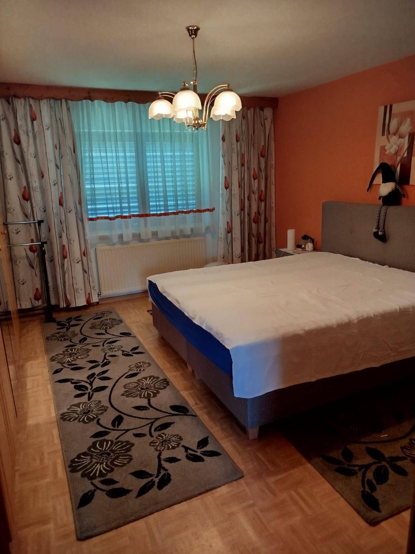 Gemütliches Schlafzimmer mit Doppelbett, orangefarbenen Wänden und Holzparkettboden.
