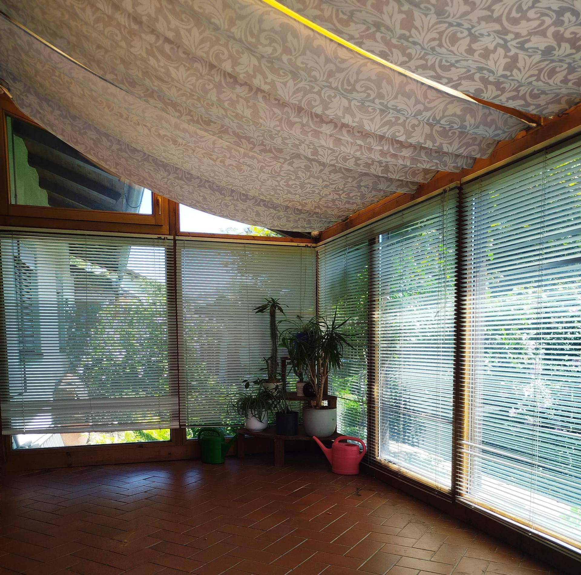 Heller Wintergarten mit großen Fenstern, Jalousien und Terrakotta-Fliesenboden, ideal für Pflanzen.
