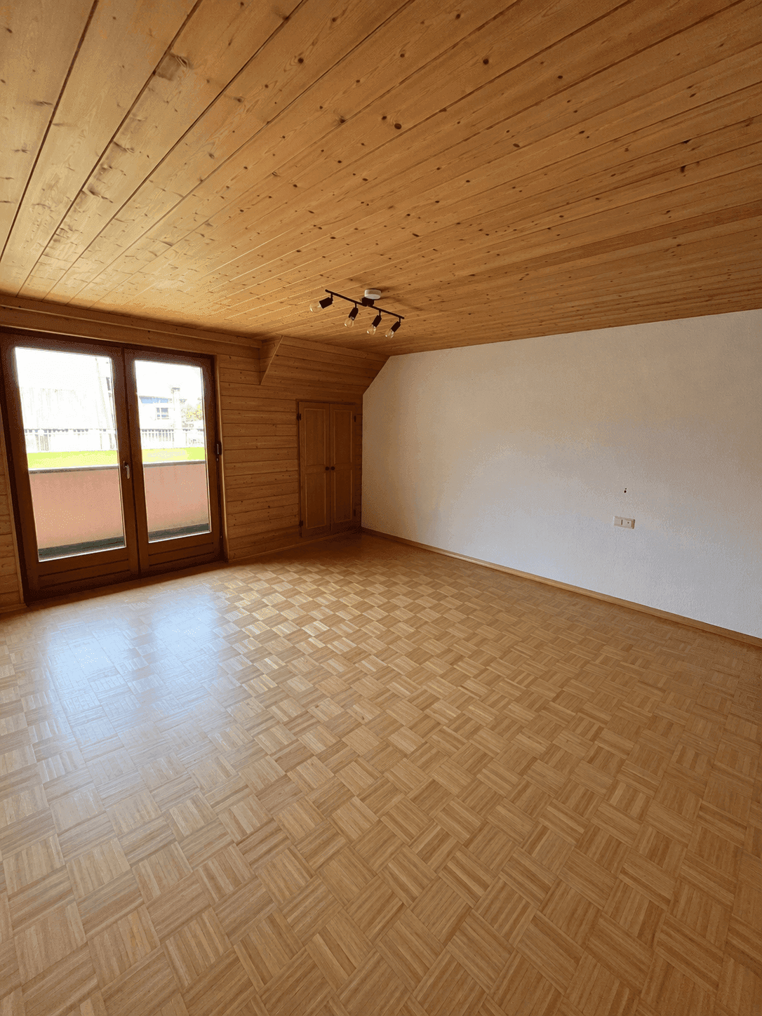 Heller Wohnraum mit Holzdecke, Parkettboden und Zugang zu einem kleinen Balkon.
