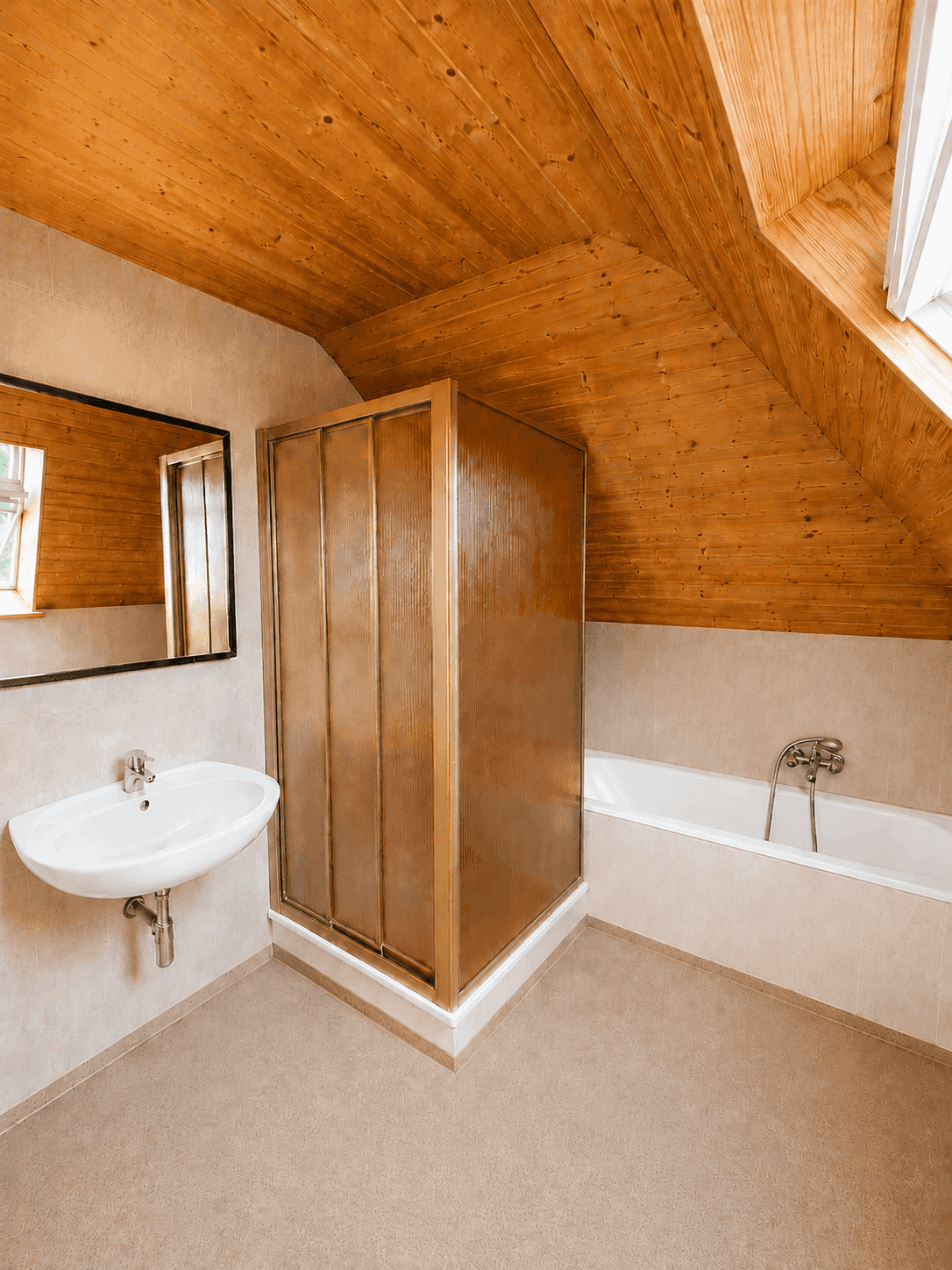 Badezimmer im Dachgeschoss mit Dusche, Badewanne, Waschbecken und Holzverkleidung an der Decke.