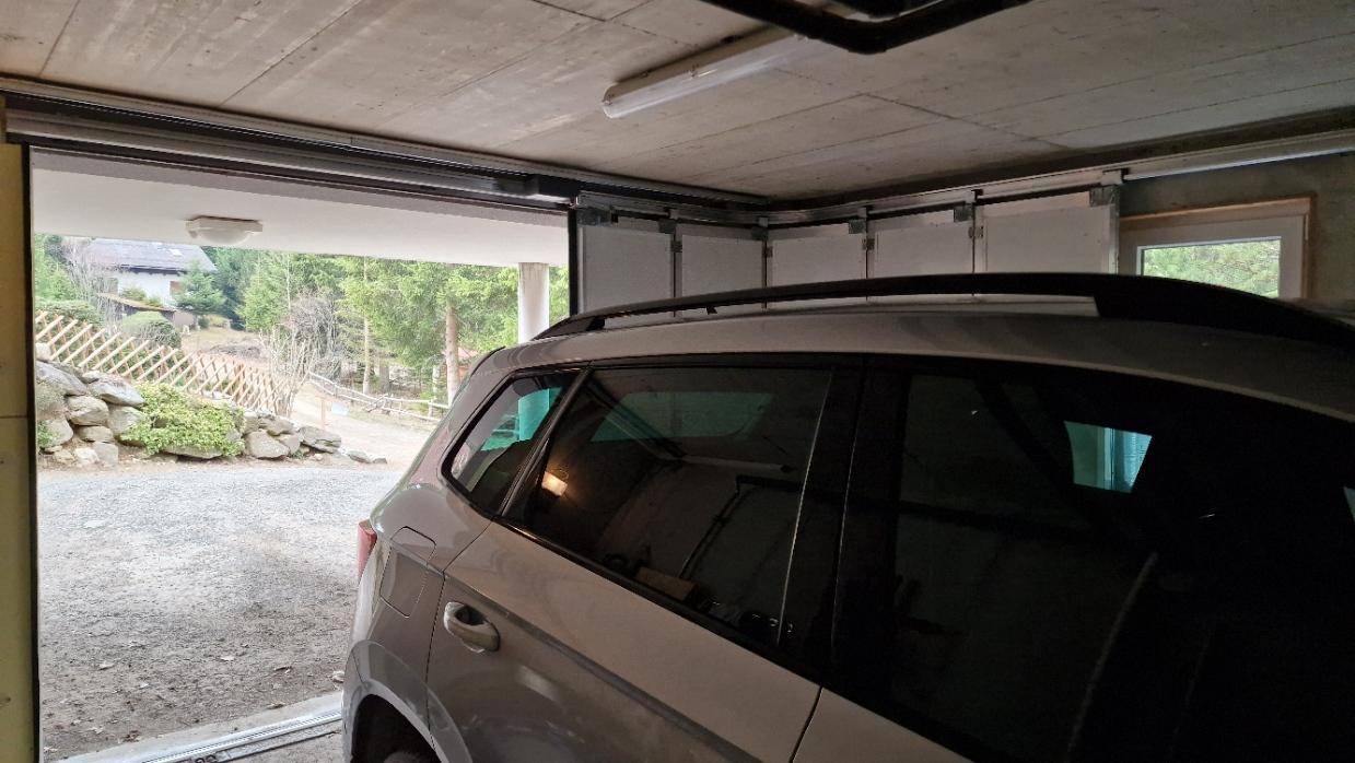 Geräumige Garage mit einem geparkten Auto und Blick auf die bewaldete Umgebung.