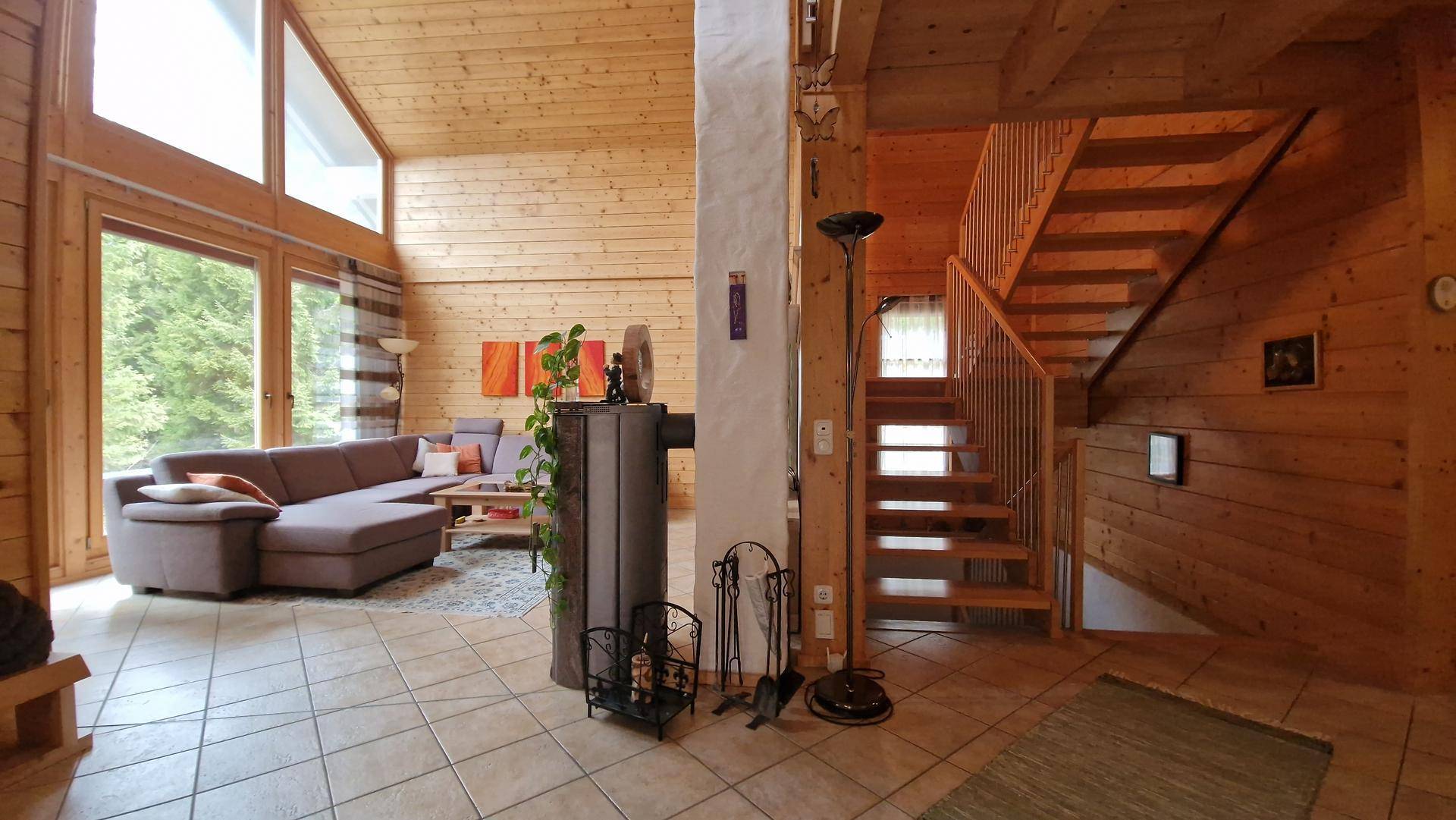 Helles Wohnzimmer mit hohen Decken, großen Fenstern und einer Holztreppe, die in die obere Etage führt.
