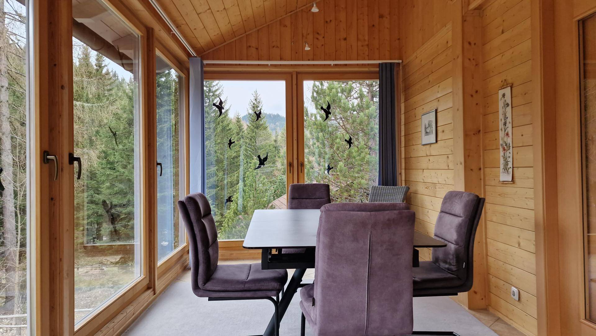 Gemütlicher Wintergarten mit Essbereich und Panoramablick auf den dichten Wald und die grüne Umgebung.