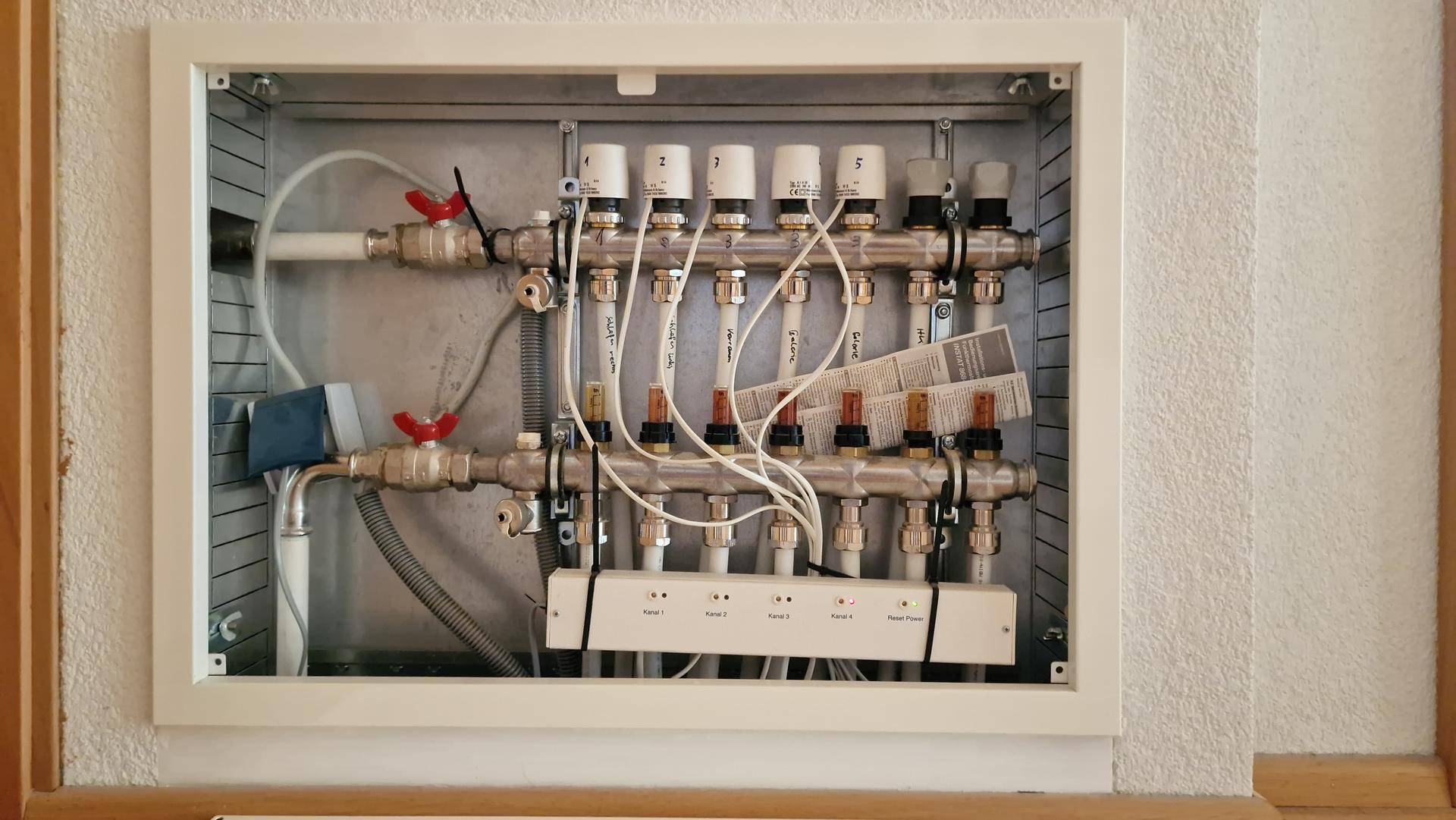 Verteilerkasten für die Fußbodenheizung mit zahlreichen Rohren und Ventilen an der Wand.
