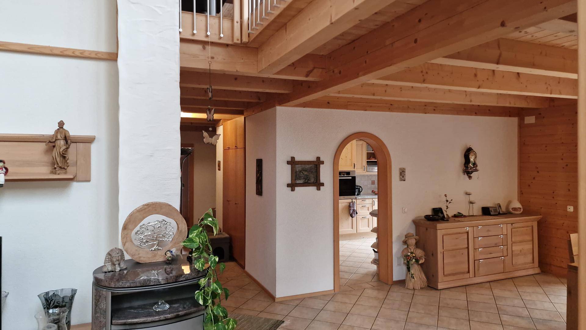 Geräumiger Wohnbereich mit Holzbalkendecke, Fliesenboden und Zugang zur Küche.