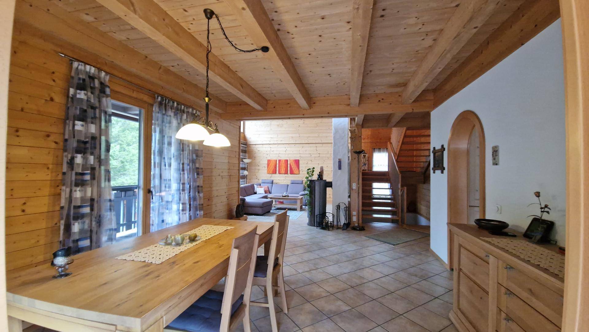 Geräumiger Wohn- und Essbereich mit Holzbalkendecke, Fliesenboden und Kaminofen.