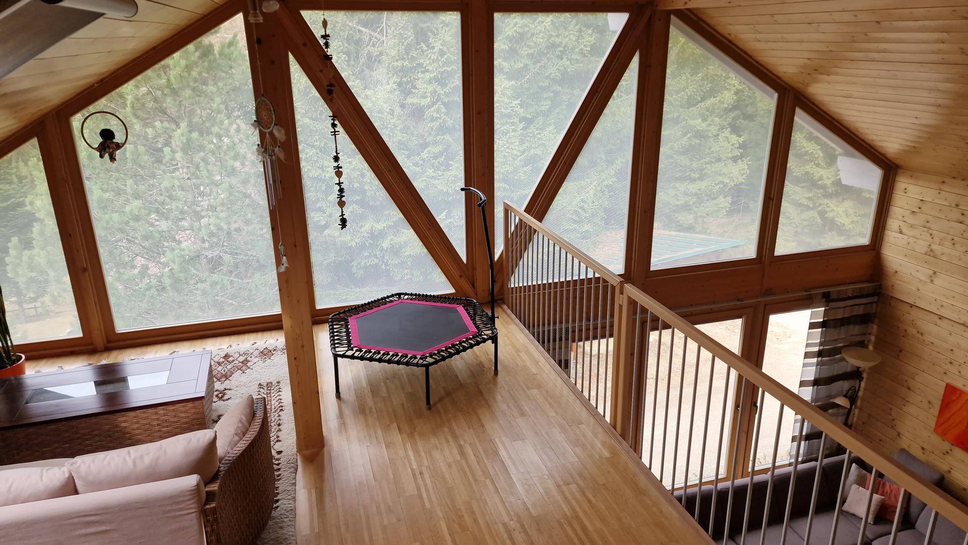 Heller Galeriebereich mit Trampolin und Sitzgelegenheit, umgeben von großen Fenstern und Holzvertäfelung.