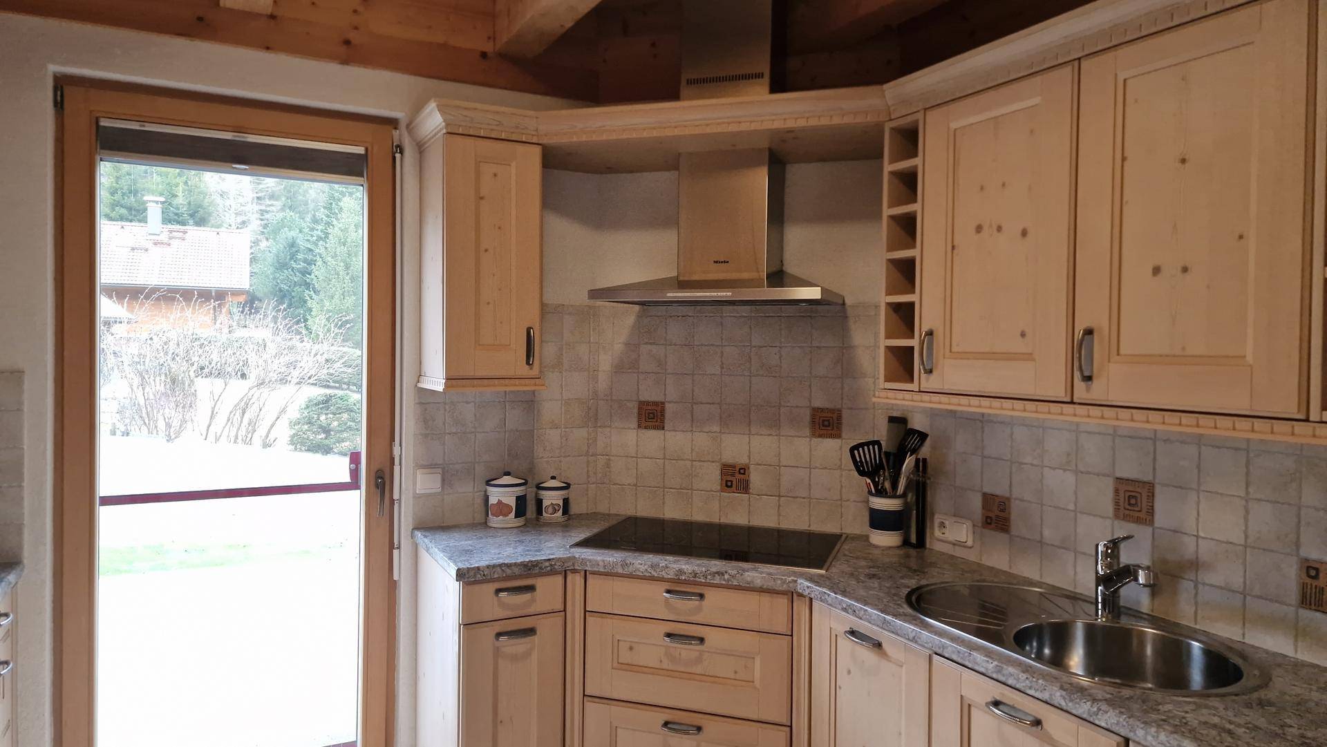 Funktionale Holzküche mit Spüle, Induktionskochfeld und Ausgang zum Außenbereich.
