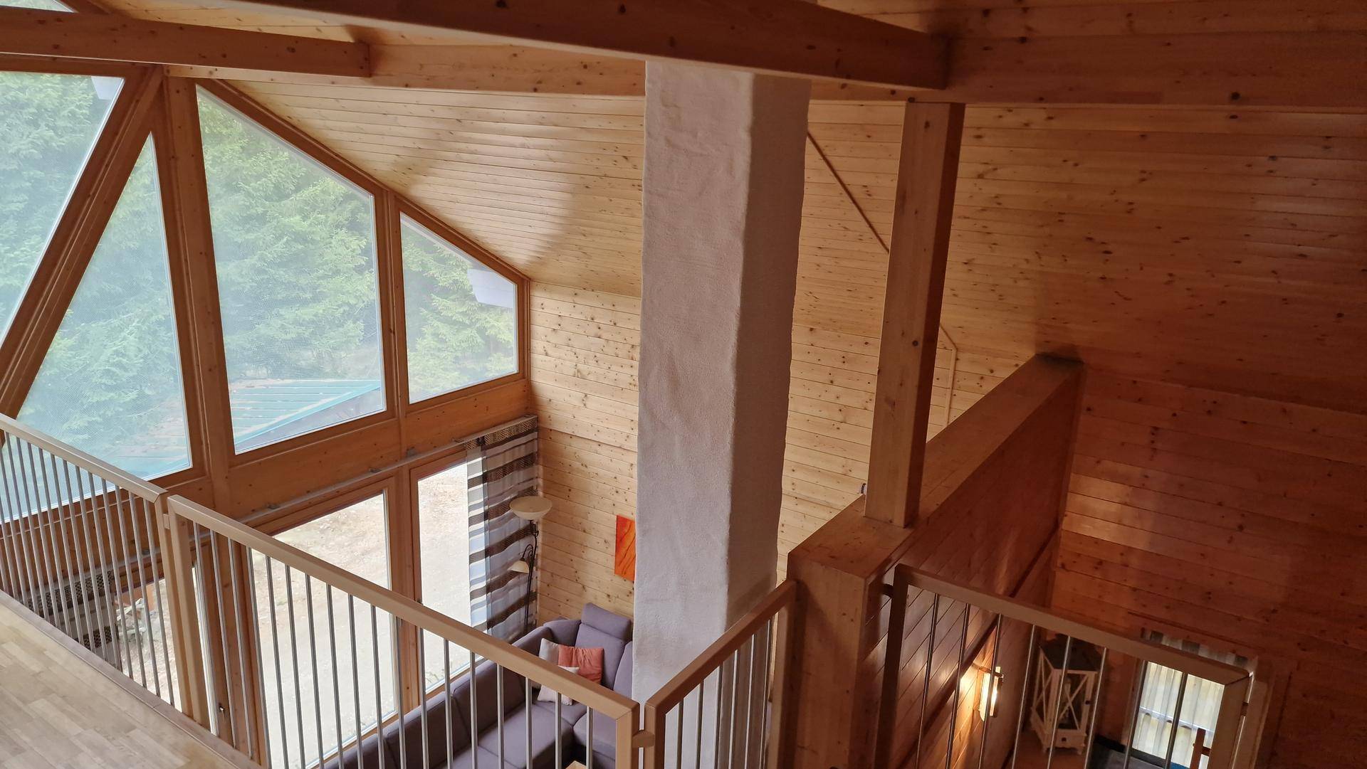 Geräumiger Wohnbereich mit hohen Holzdecken, großen Fenstern und Blick ins Grüne.