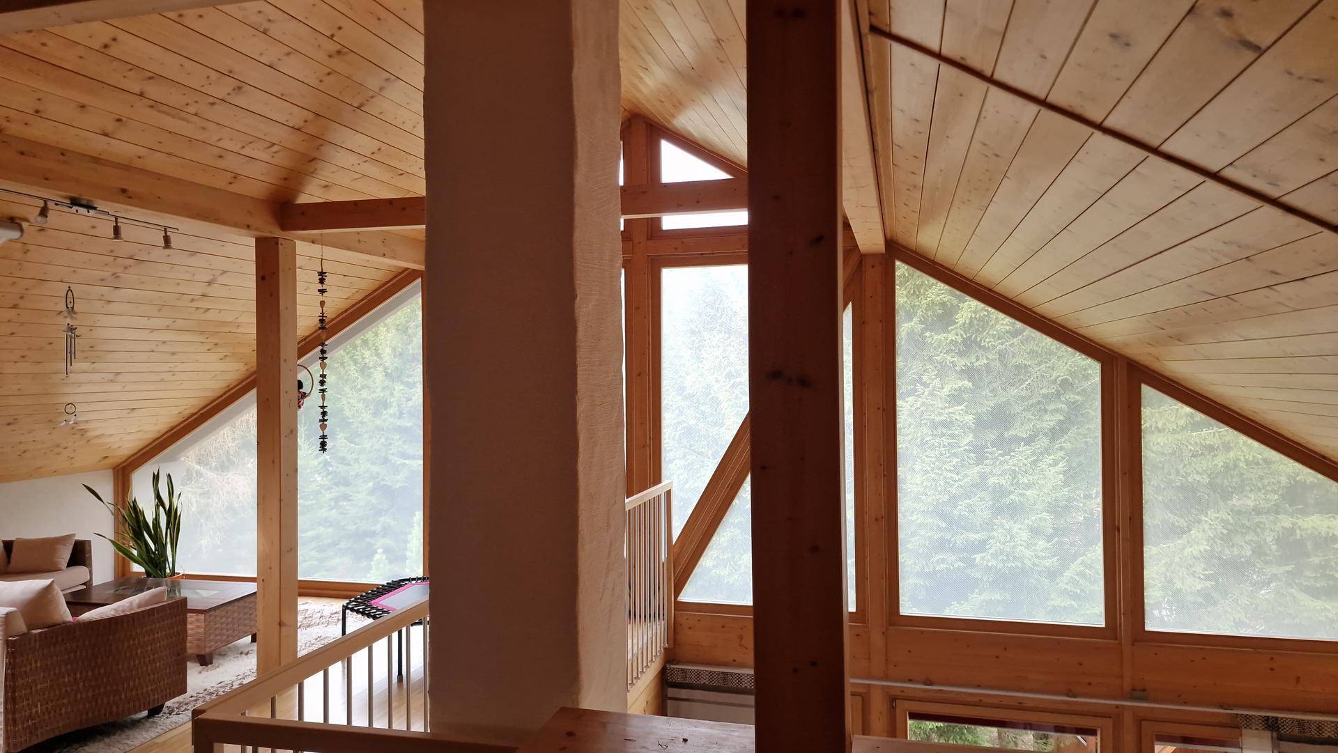 Heller Wohnbereich im Dachgeschoss mit hohen Decken und großen Fenstern mit Waldblick.