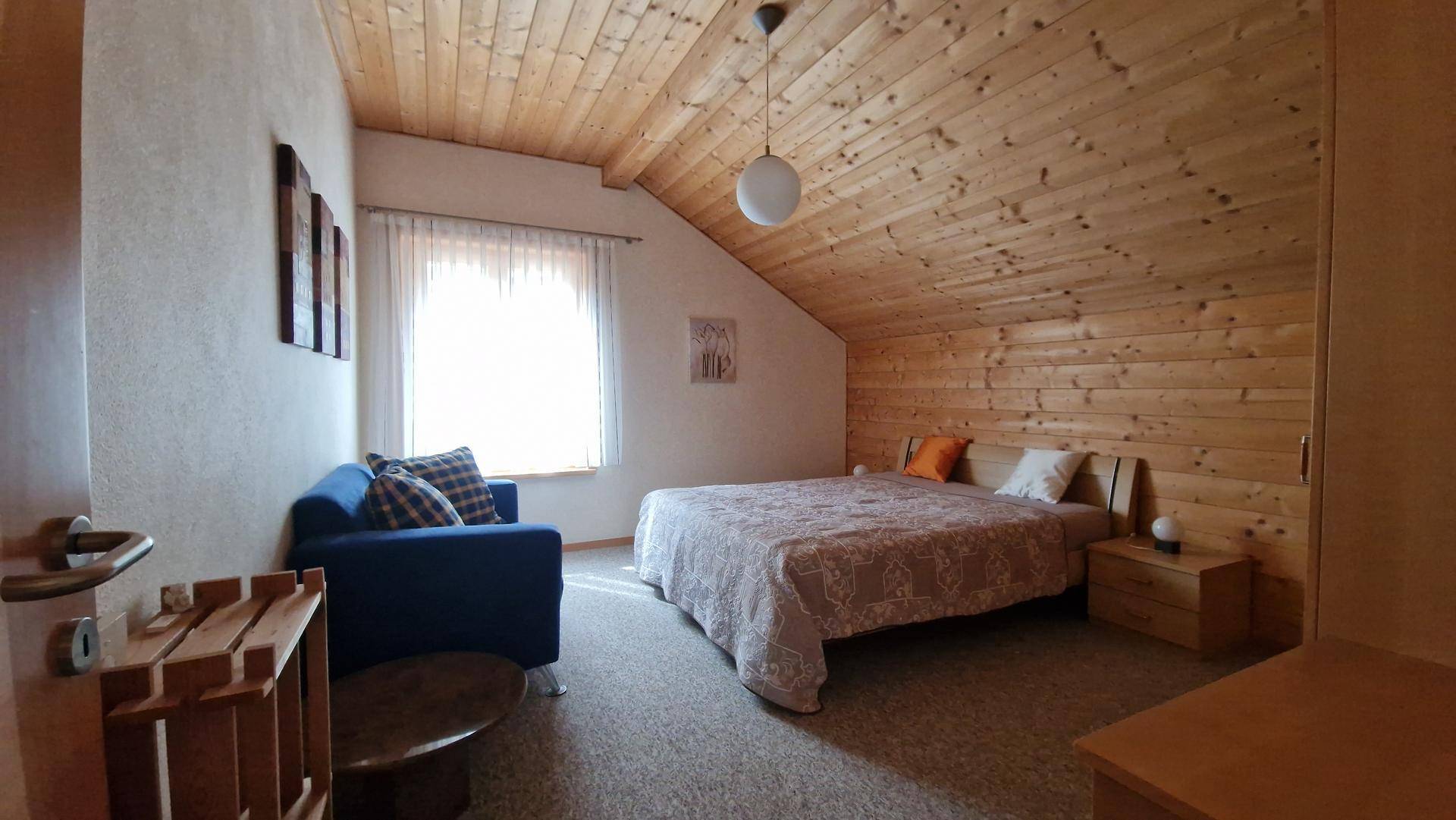 Helles Schlafzimmer mit Holzverkleidung, Doppelbett und einem kleinen Sofa unter dem Fenster.