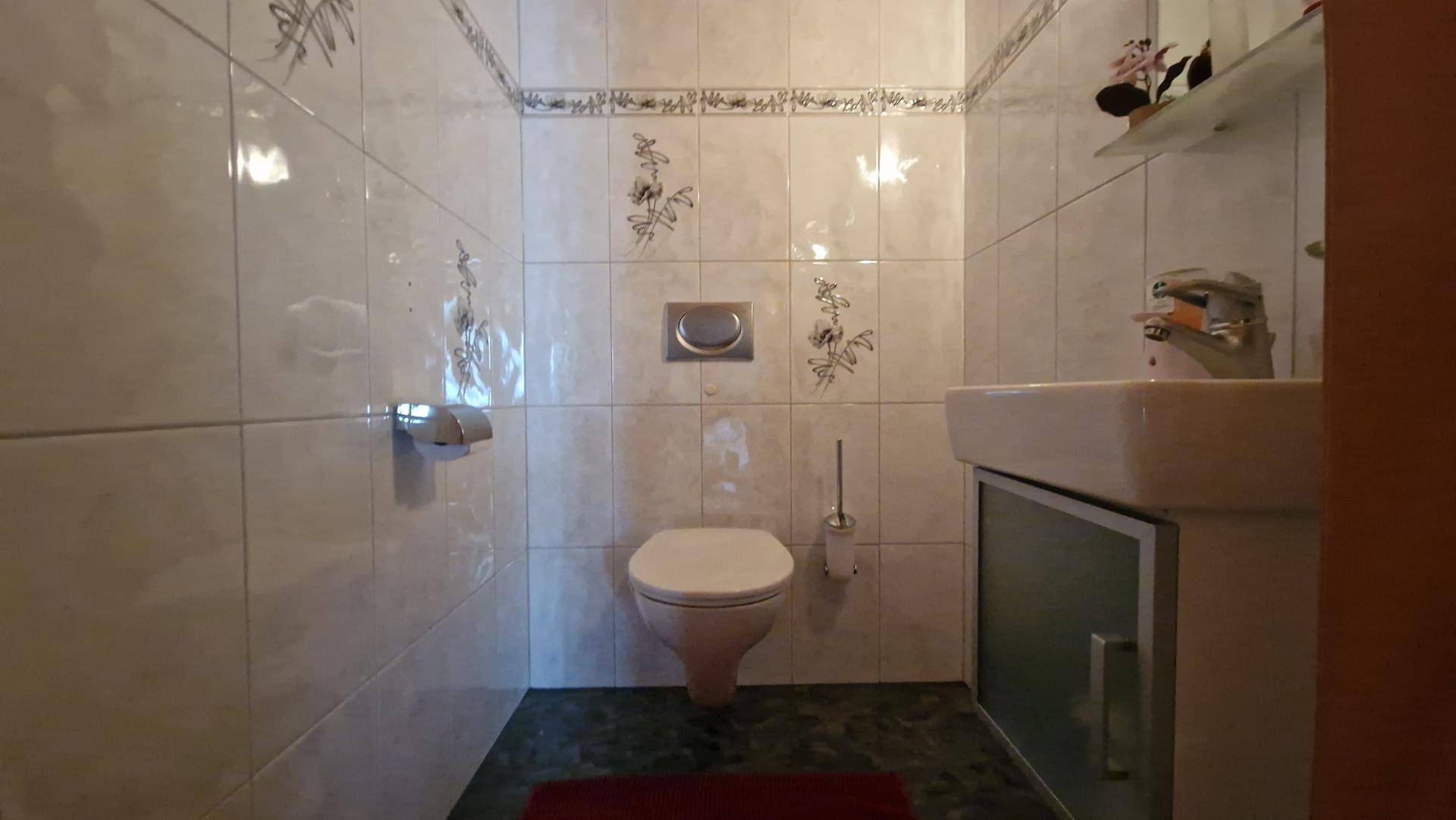 Kleines Gäste-WC mit weißen Fliesen, wandhängender Toilette und einem einzelnen Waschbecken.