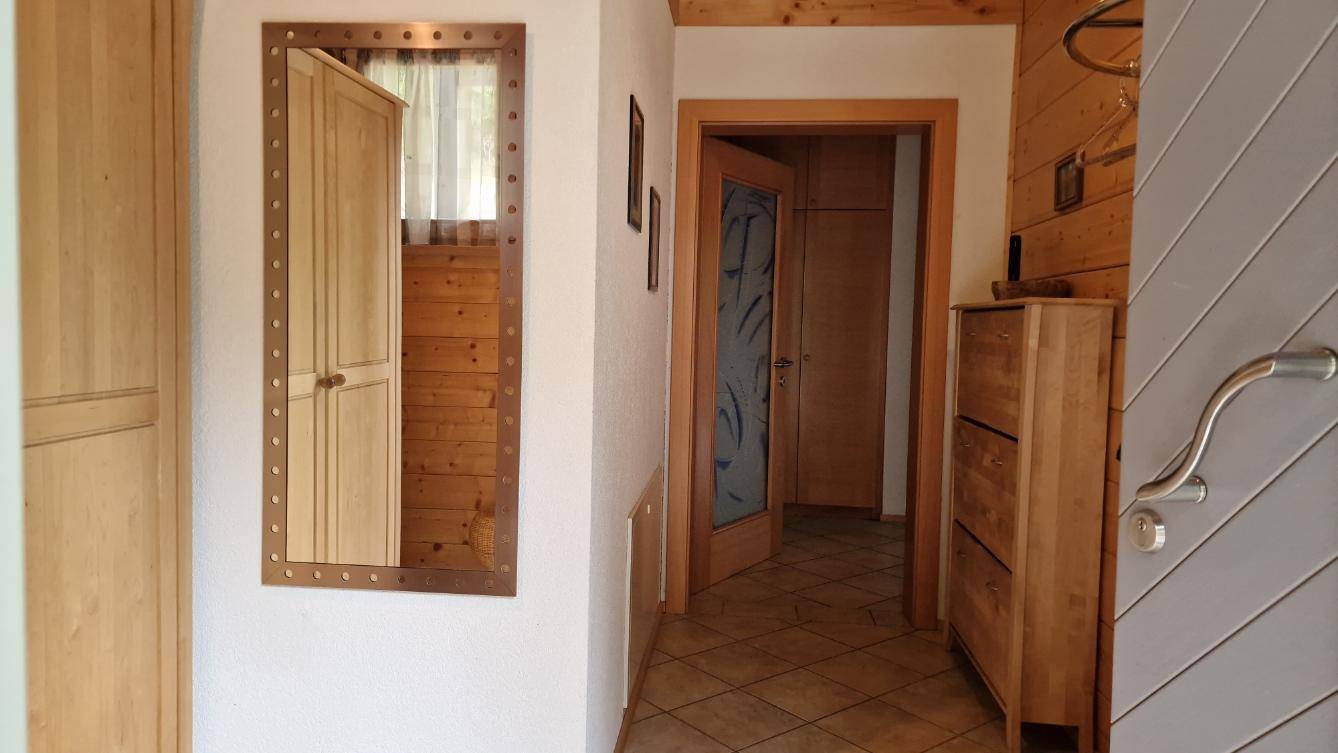 Heller Eingangsbereich mit Holzmöbeln, großem Spiegel und Fliesenboden.