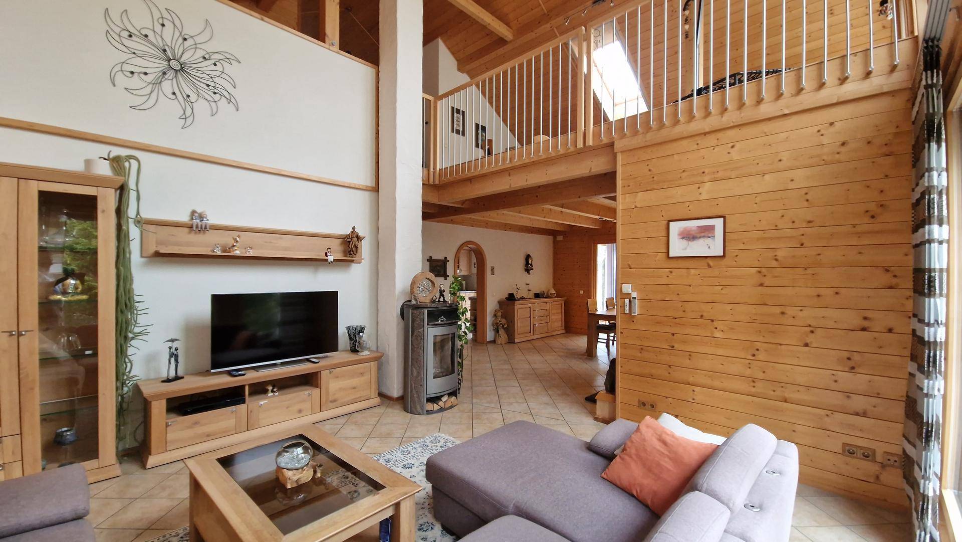Geräumiges Wohnzimmer mit hohen Decken, Holzbalken und einem gemütlichen Kaminofen, offen zur Galerie.