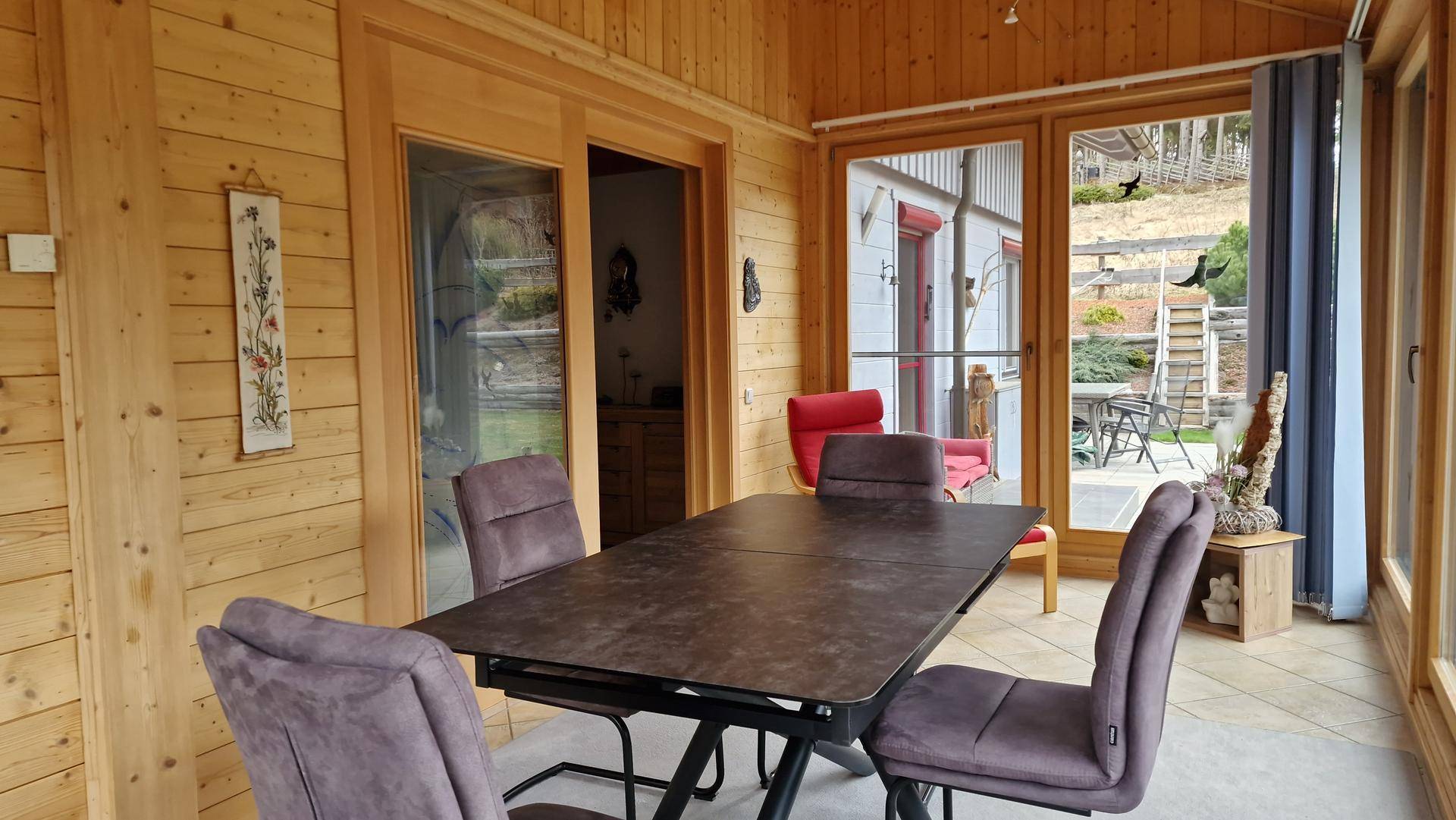 Warmer Wintergarten mit Holzwänden und Essbereich, bietet Zugang zu einem weiteren Raum und dem Außenbereich.
