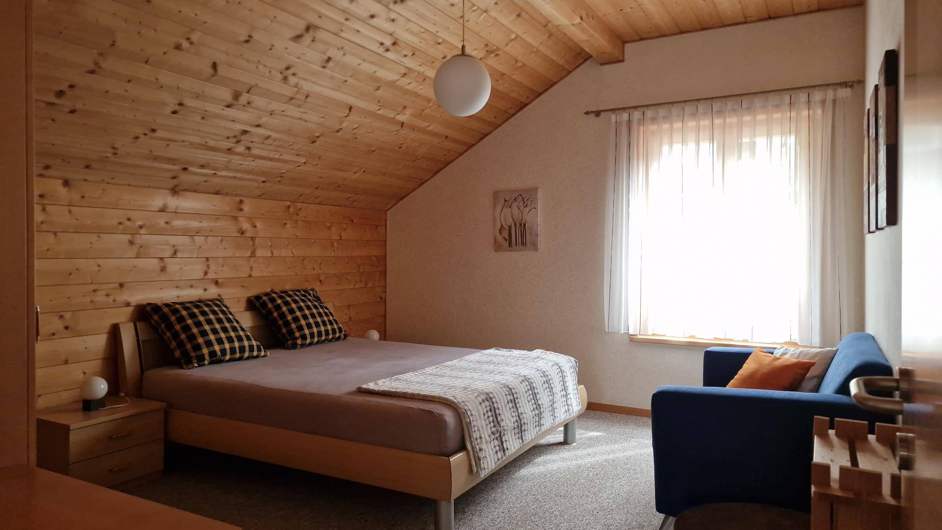 Gemütliches Schlafzimmer mit Holzvertäfelung an Wänden und Decke, Doppelbett und Fenster.