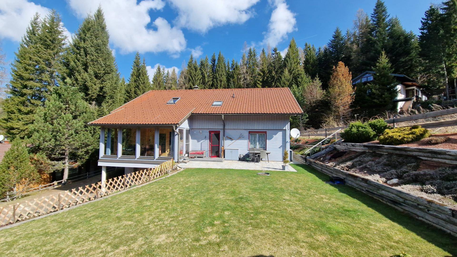 Freistehendes Haus mit rotem Ziegeldach und großem Garten in sonniger Hanglage.