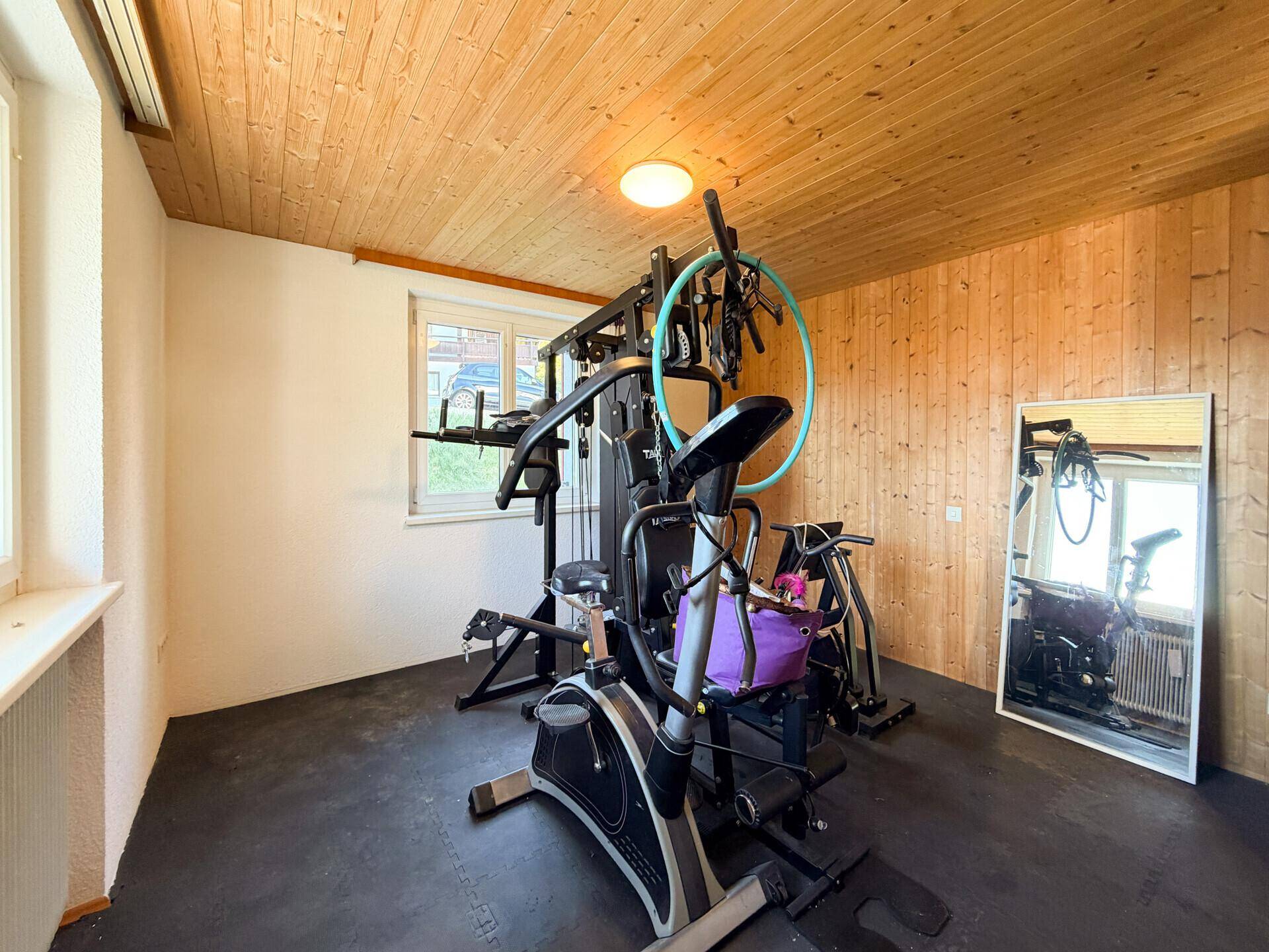 Fitnessraum mit Holzdecken und -wänden, ausgestattet mit verschiedenen Trainingsgeräten für das tägliche Workout.