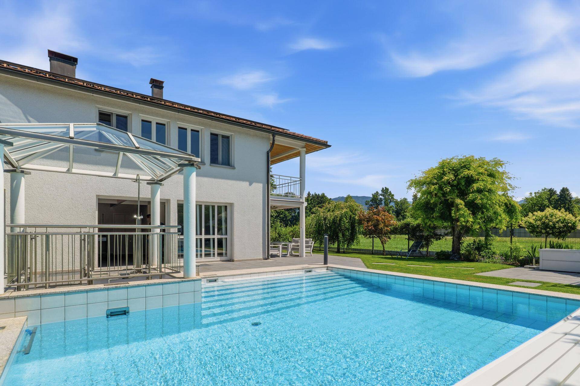 Außenansicht des Hauses mit großem Pool und angrenzender Grünfläche.