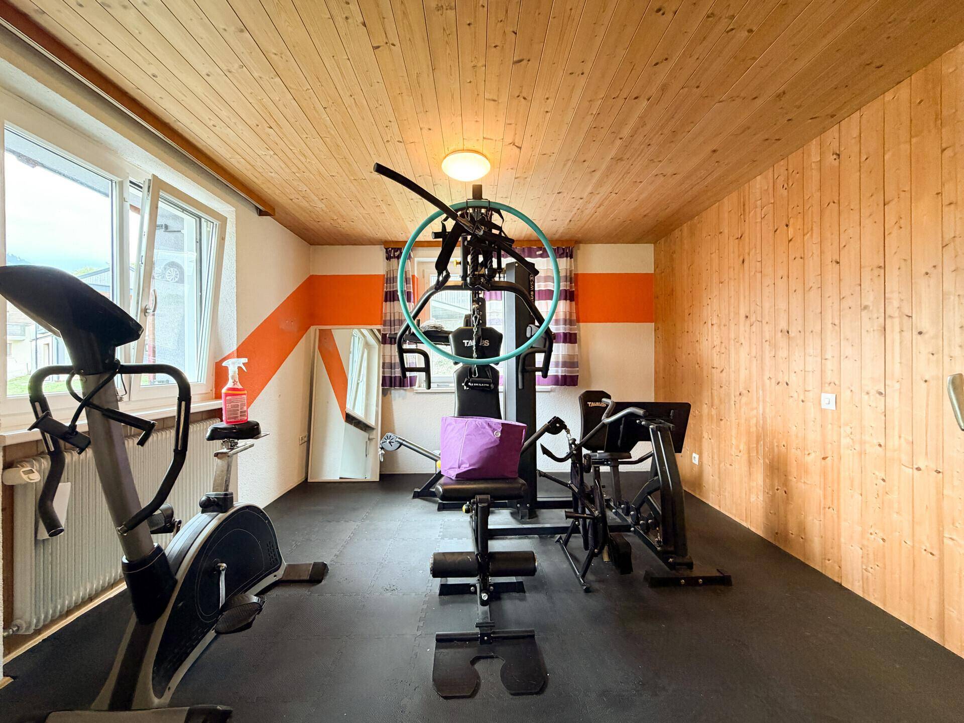 Gut ausgestatteter Fitnessraum mit Holzverkleidung, Gummiboden und verschiedenen Trainingsgeräten.