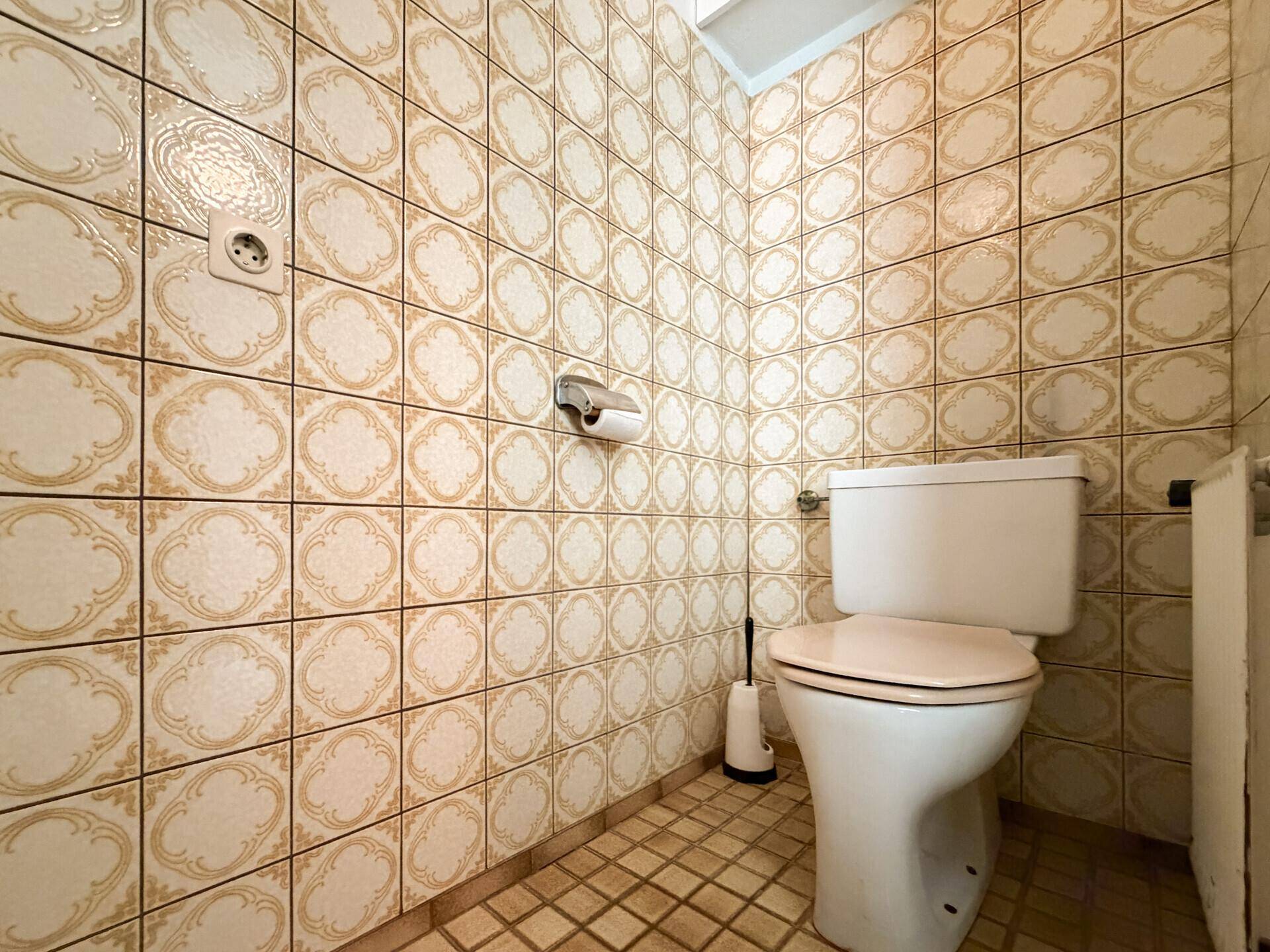 Kleines Gäste-WC mit gemusterten Fliesen an Wänden und Boden sowie einer Toilette.