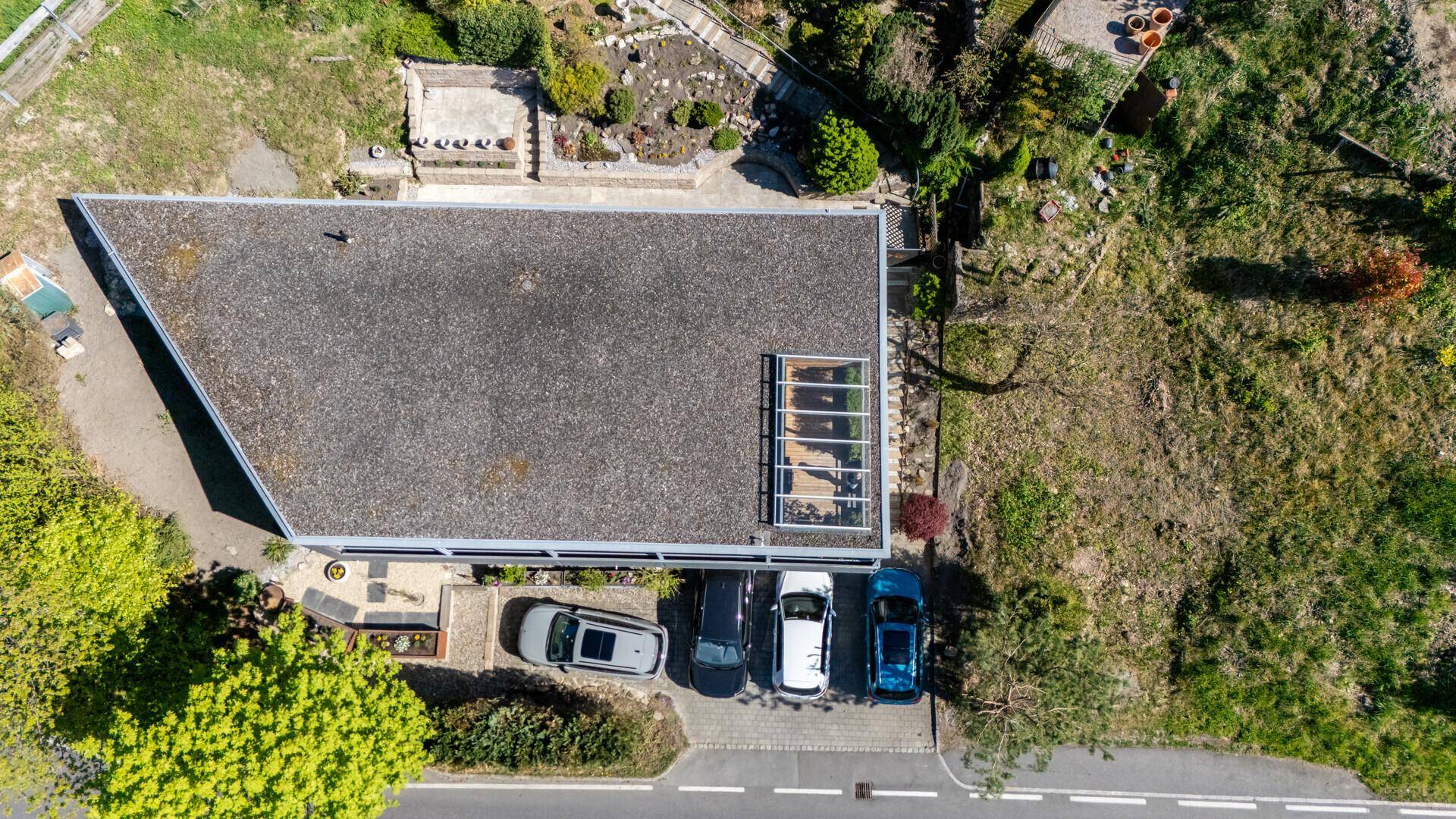 Draufsicht auf das Flachdach des Hauses mit Oberlichtern und geparkten Autos davor.