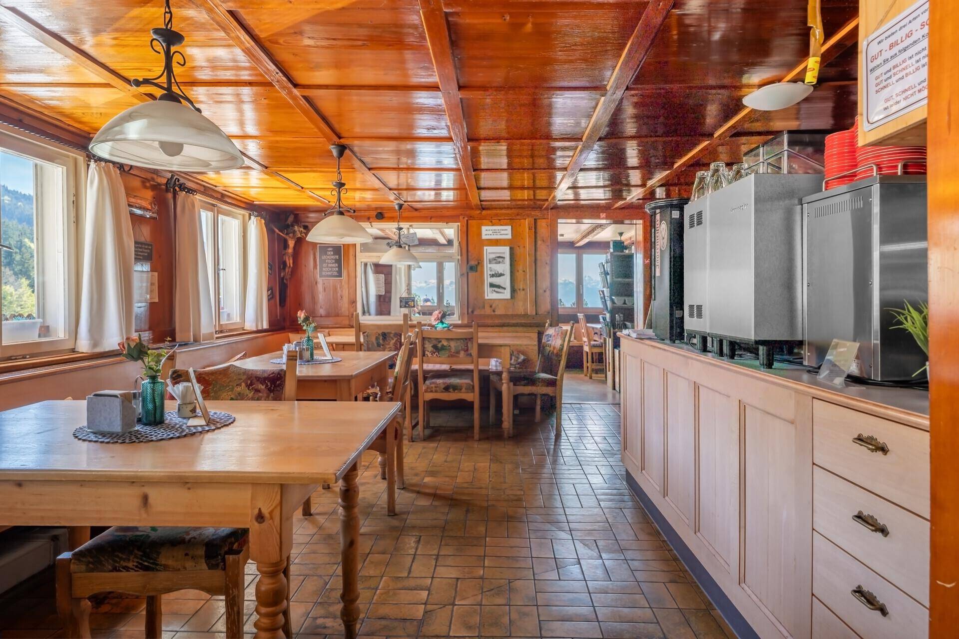 Rustikaler Speisesaal mit Holztäfelung an Decke und Wänden, traditionellen Tischen und Stühlen sowie einer Theke.