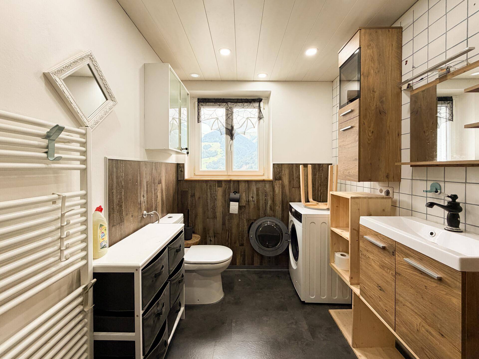 Funktionales Badezimmer mit Toilette, Waschbecken, Waschmaschine und beheiztem Handtuchhalter.