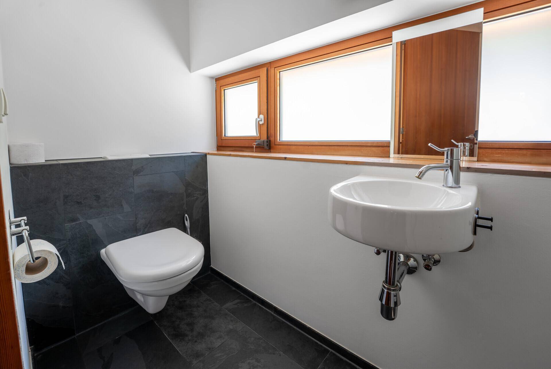 Kleines Gäste-WC mit Wand-WC, Waschbecken und Fenster.