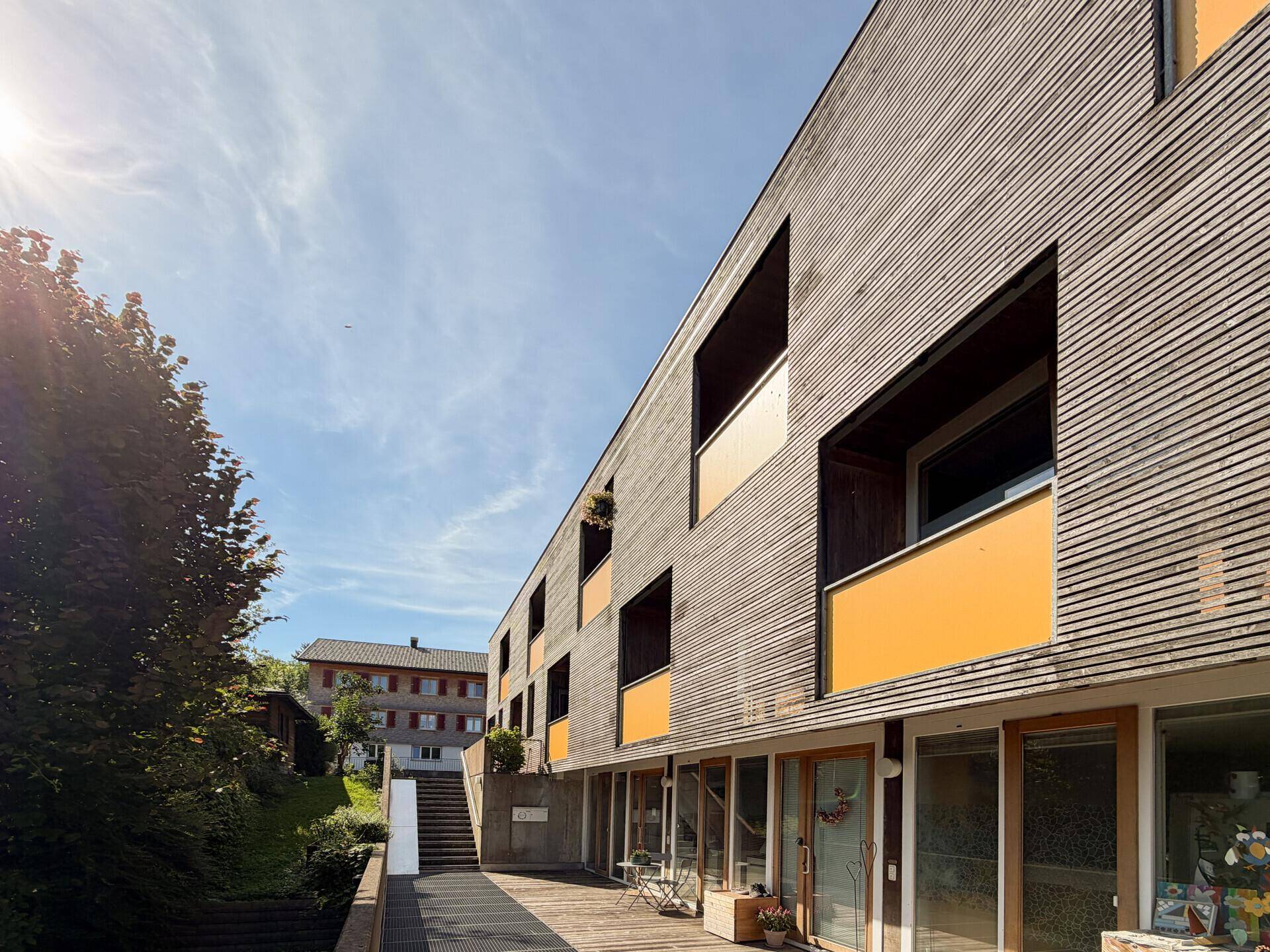 Moderne Architektur des Gebäudes mit Holzfassade und gelben Akzenten unter blauem Himmel.