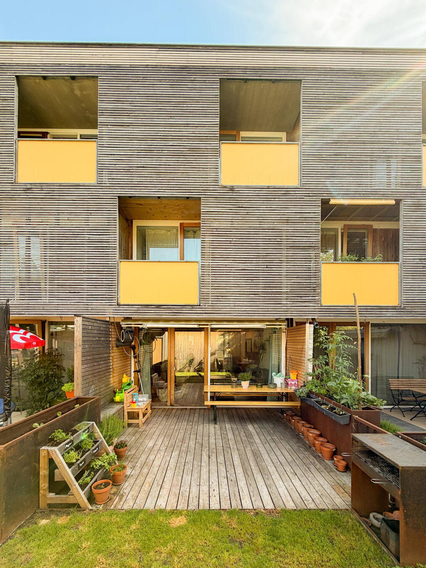 Moderner Gartenbereich mit Holzterrasse, Hochbeeten und Grillplatz.