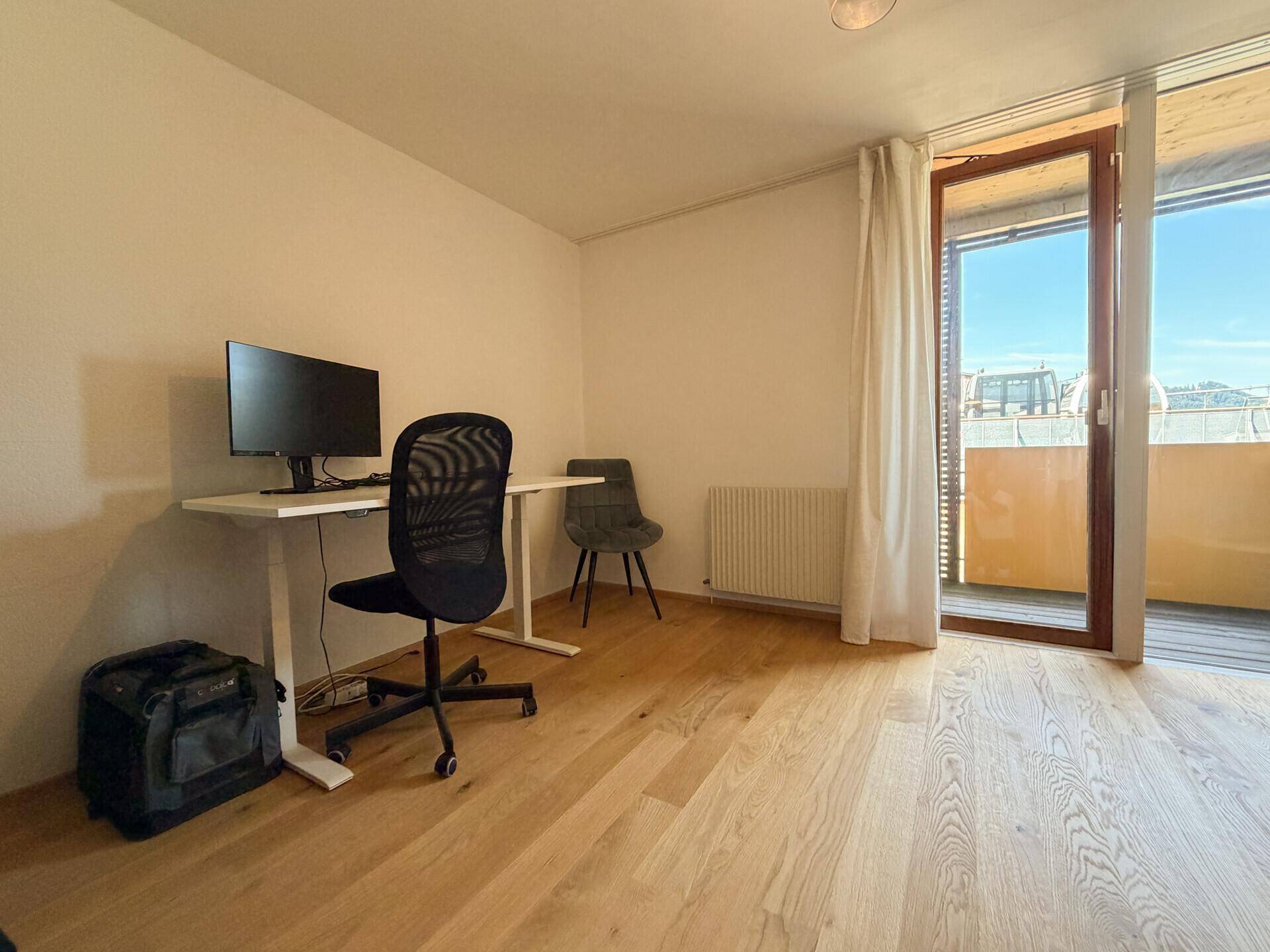 Helles Arbeitszimmer mit Schreibtisch, Bürostuhl und Zugang zu einem Balkon.