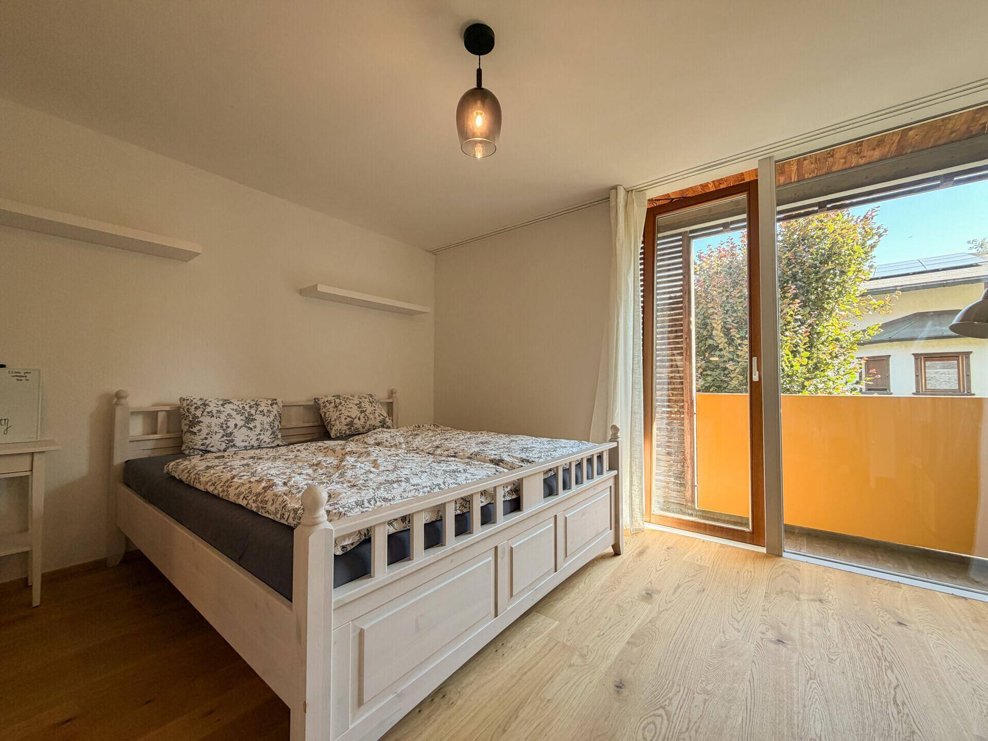 Schlafzimmer mit Doppelbett, Holzboden und direktem Zugang zu einem Balkon.