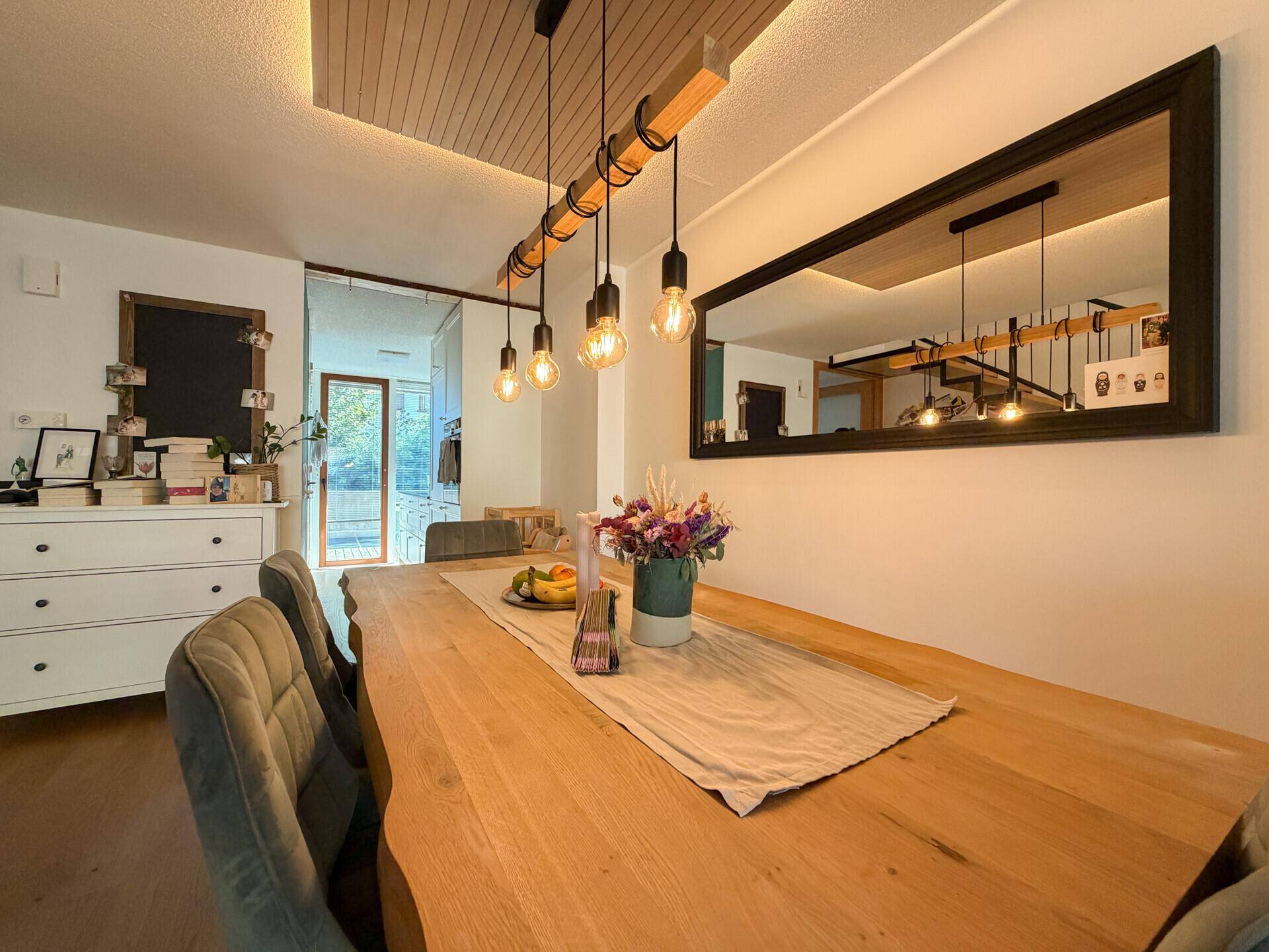Stilvoller Essbereich mit massivem Holztisch, Samtstühlen und großem Wandspiegel.