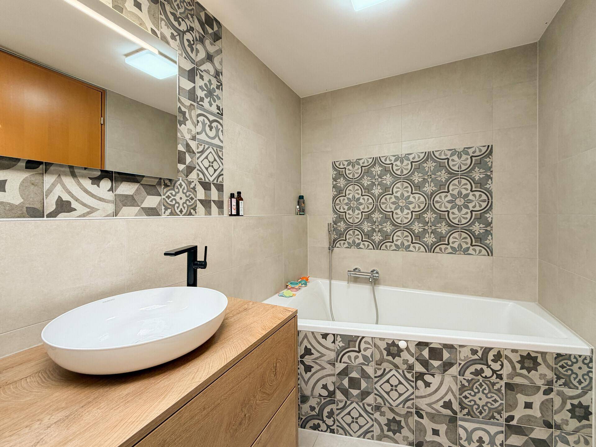 Badezimmer mit Badewanne, modernem Waschtisch und dekorativen Fliesen.