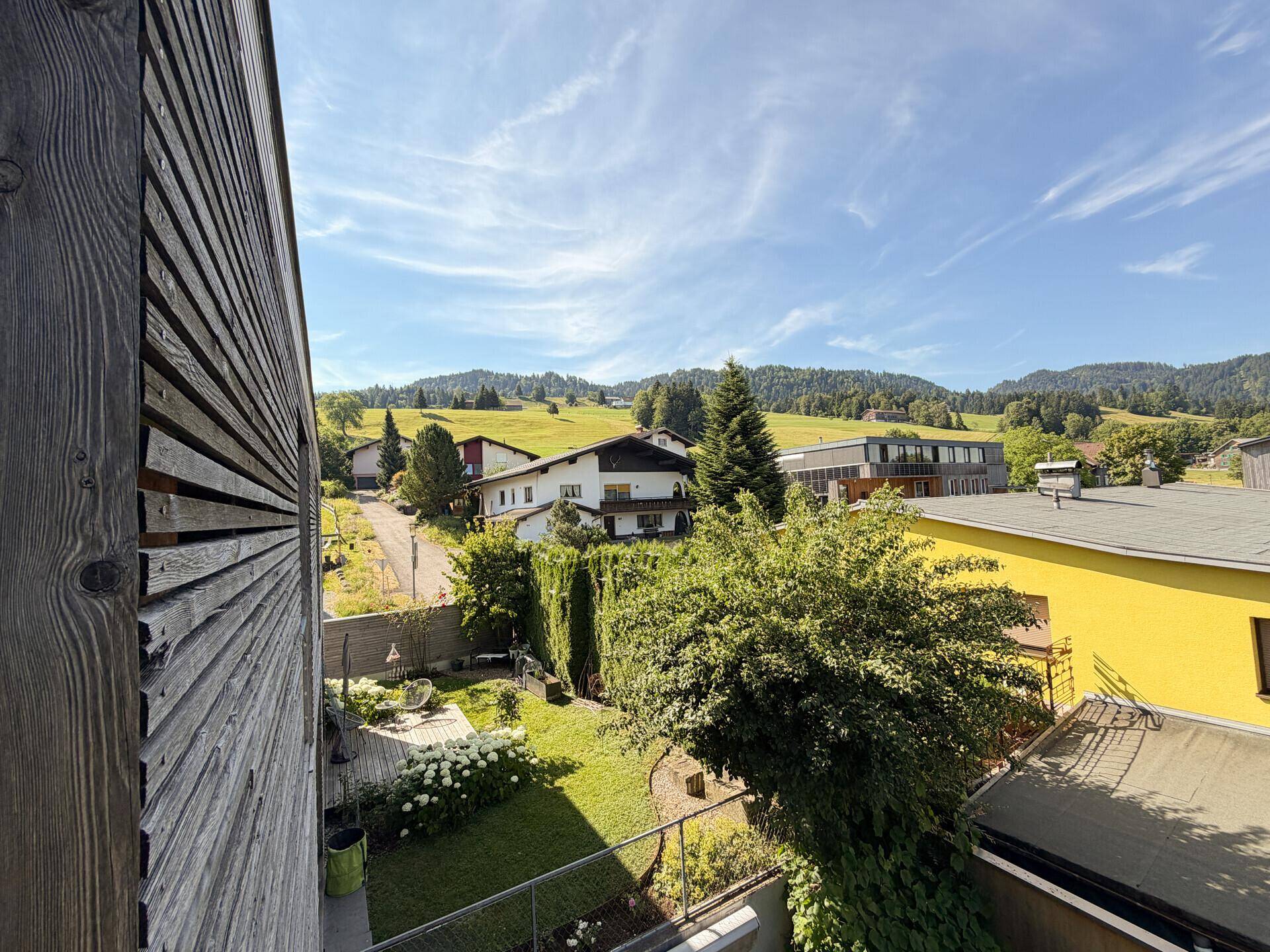 Weitläufiger Blick vom Balkon auf die grüne Landschaft und umliegende Häuser.