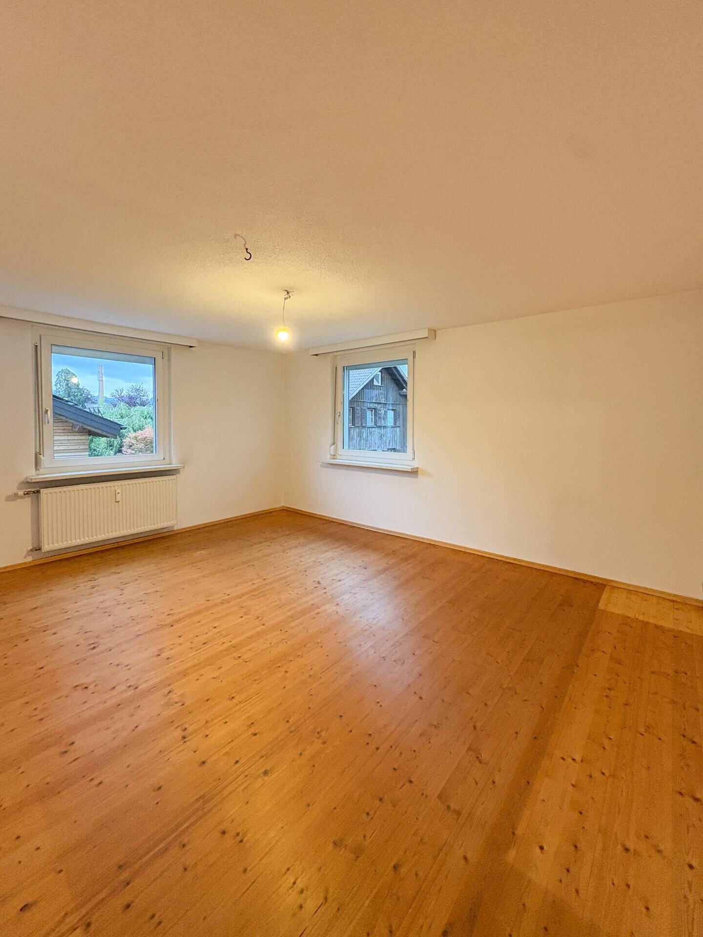 Geräumiges Zimmer mit Holzfußboden und zwei Fenstern, die Tageslicht hereinlassen.