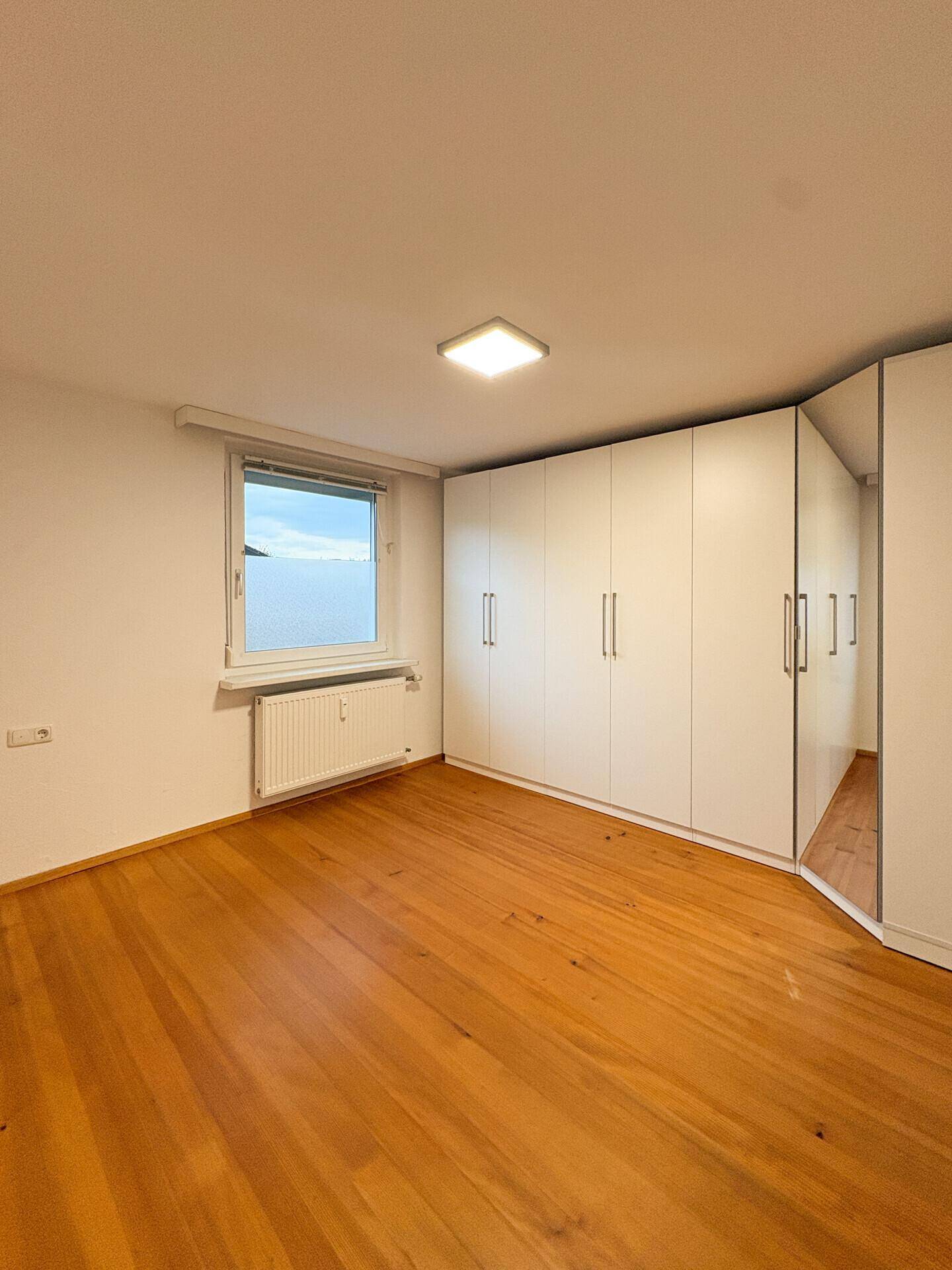 Schlafzimmer mit großem weißen Einbauschrank, hellem Holzfußboden und Fenster.