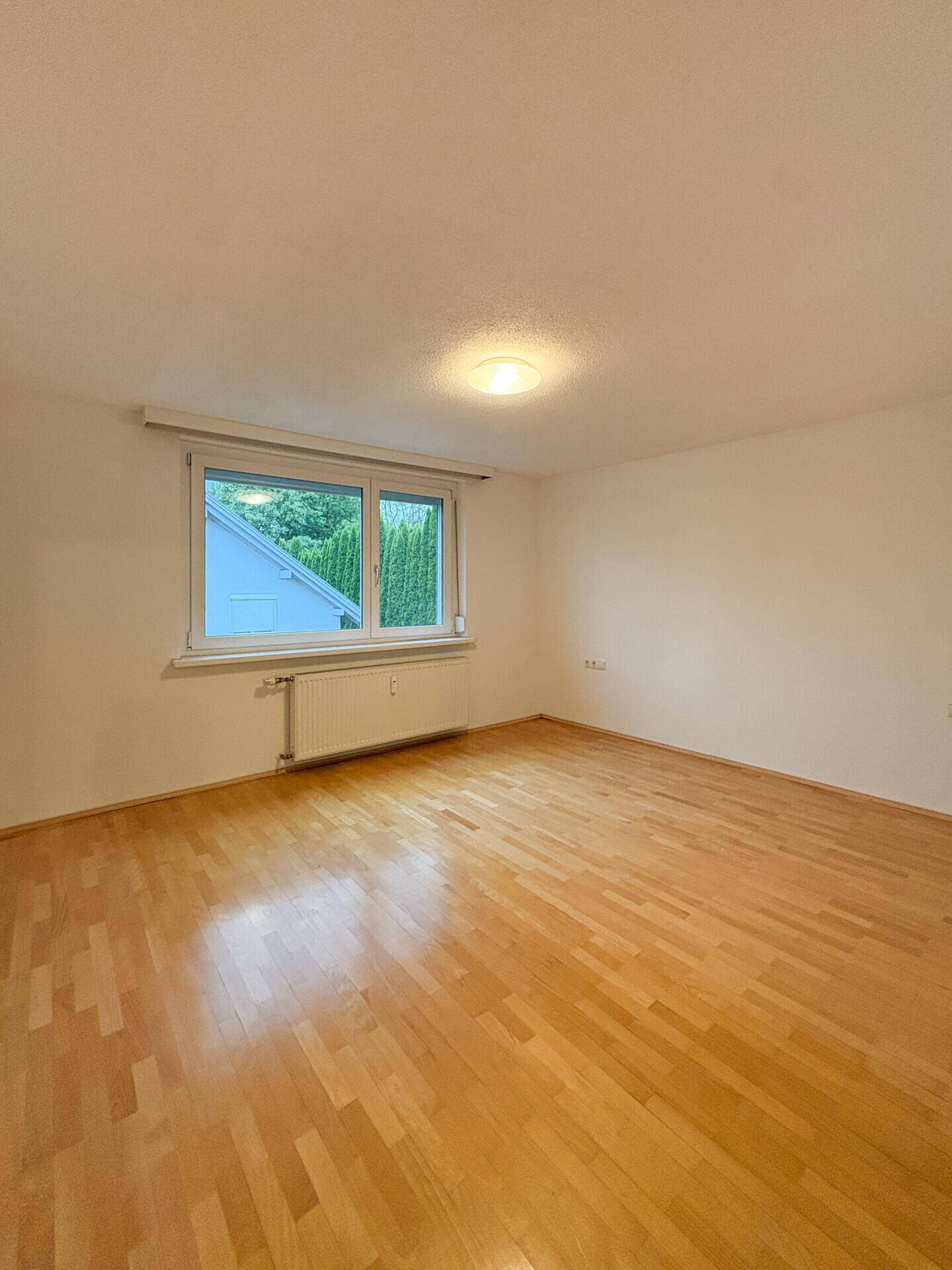 Helles Zimmer mit Holzfußboden und Blick ins Grüne durch das Fenster.