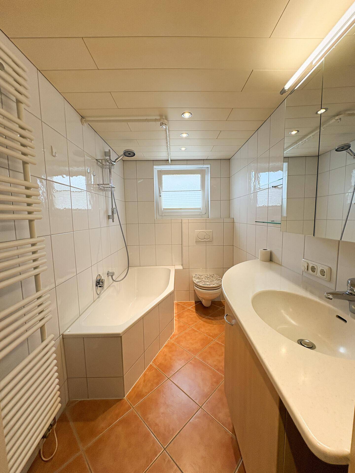 Gefliestes Badezimmer mit Badewanne, WC, Waschbecken und beheiztem Handtuchhalter.