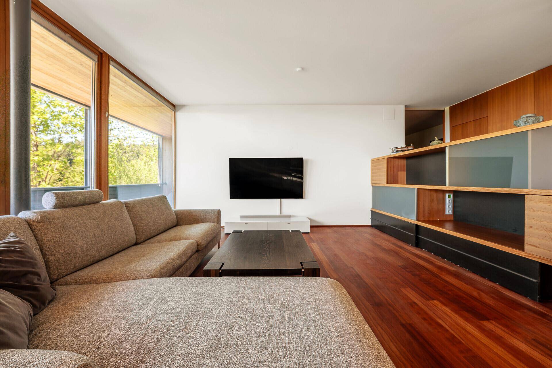 Geräumiges Wohnzimmer mit großem Sofa, Fernseher und Holzboden, bietet viel natürliches Licht.