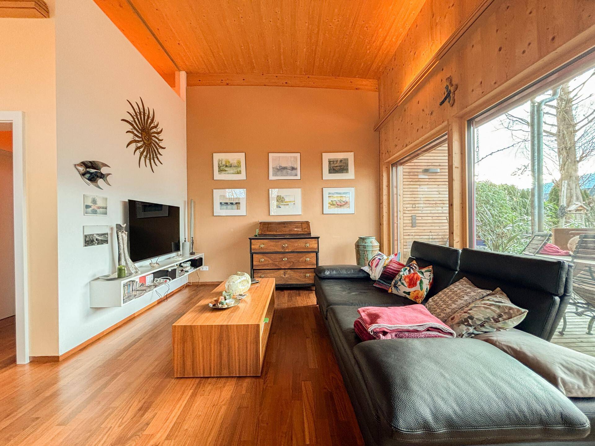 Moderner Wohnbereich mit Fernseher, Holzboden und Zugang zu einer sonnigen Terrasse.