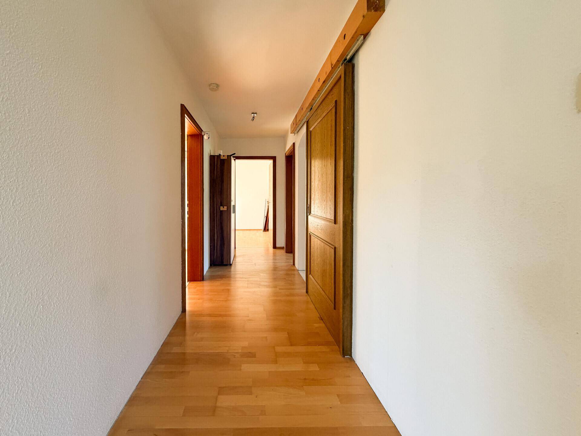 Heller Flur mit Holzparkettboden und traditionellen Holztüren, der verschiedene Räume miteinander verbindet.
