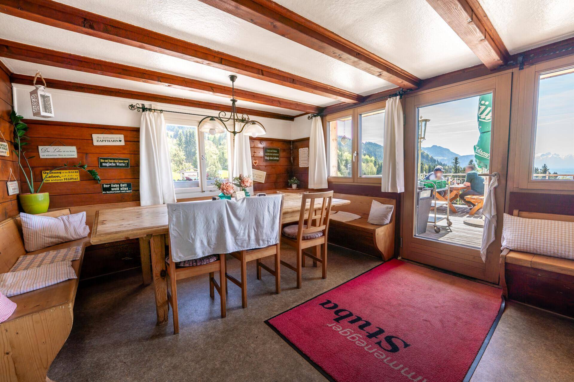 Heller Speisesaal mit Holztischen und Bänken, Zugang zu einer Außenterrasse und Blick auf die Berge.