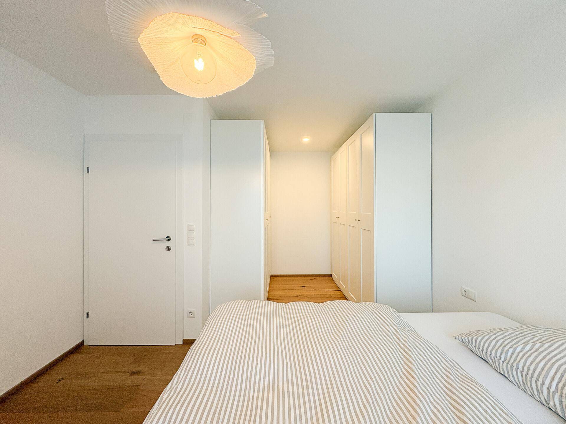 Helles Schlafzimmer mit Holzboden, weißem Bett und integrierten Kleiderschränken.