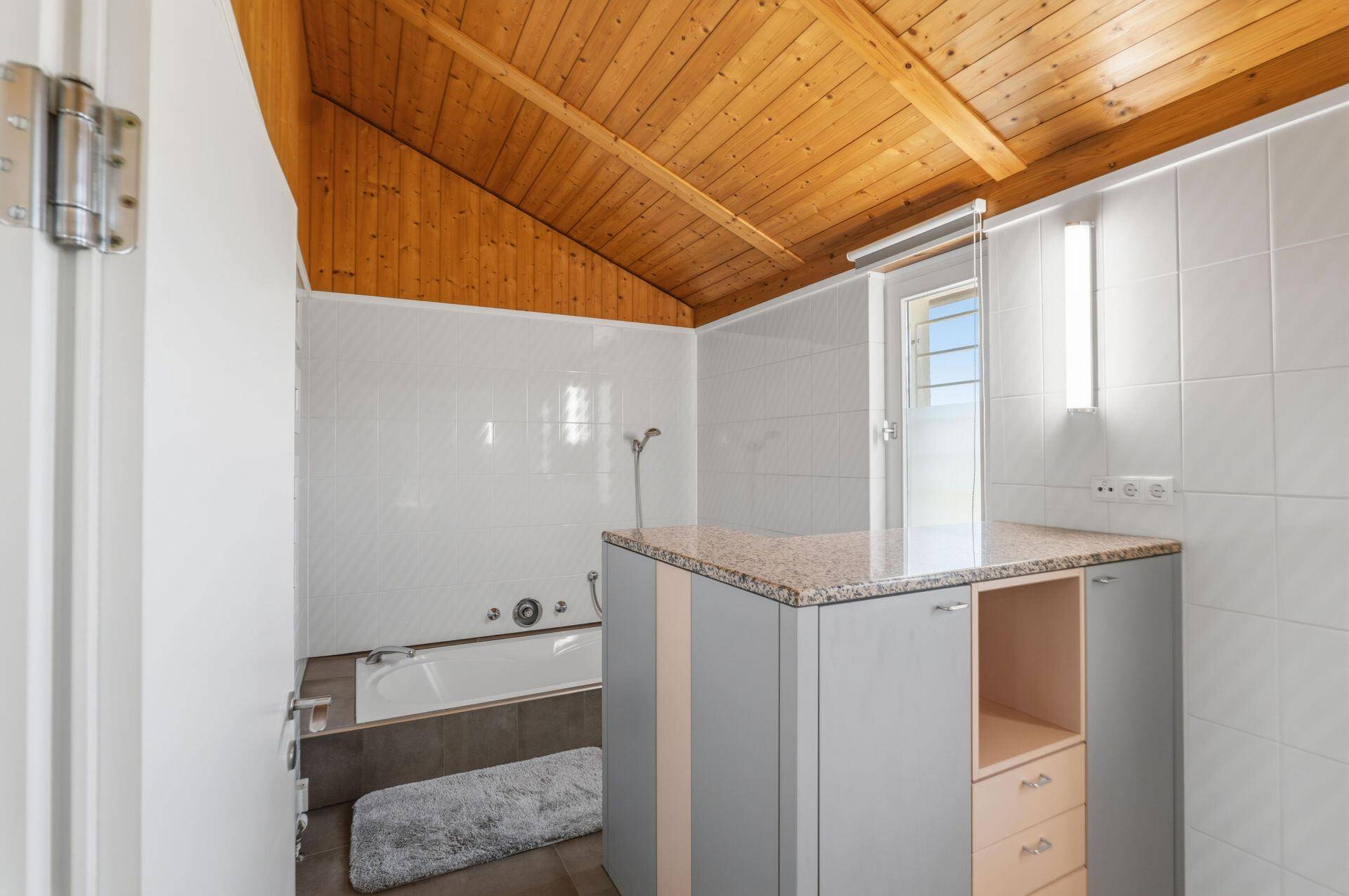 Badezimmer mit Badewanne, Holzdecke und hellen Fliesen, ausgestattet mit Granit-Arbeitsplatte.