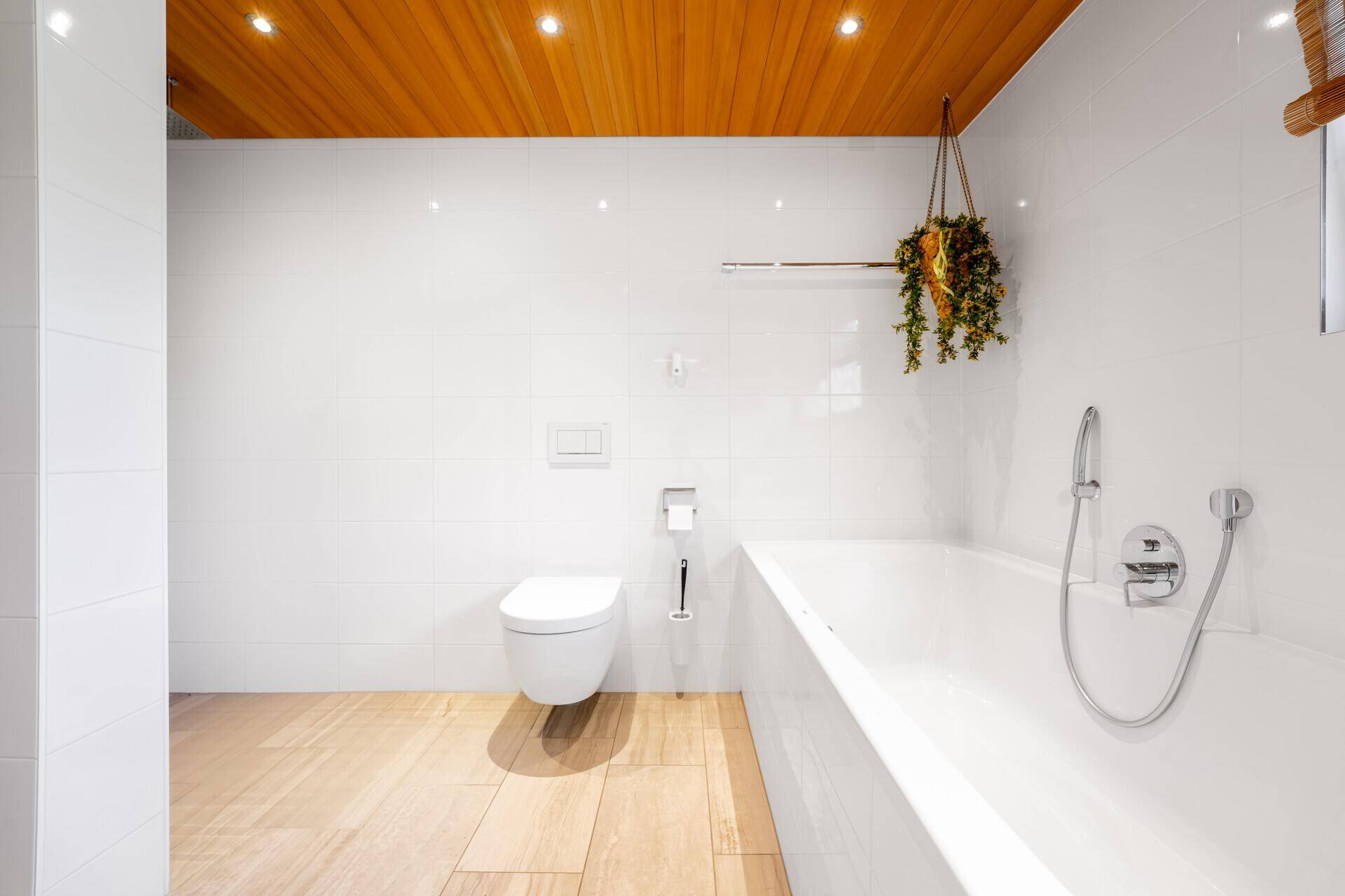 Modernes Badezimmer mit weißen Fliesenwänden, Wandtoilette und Badewanne, sowie Holzoptik-Fliesenboden.
